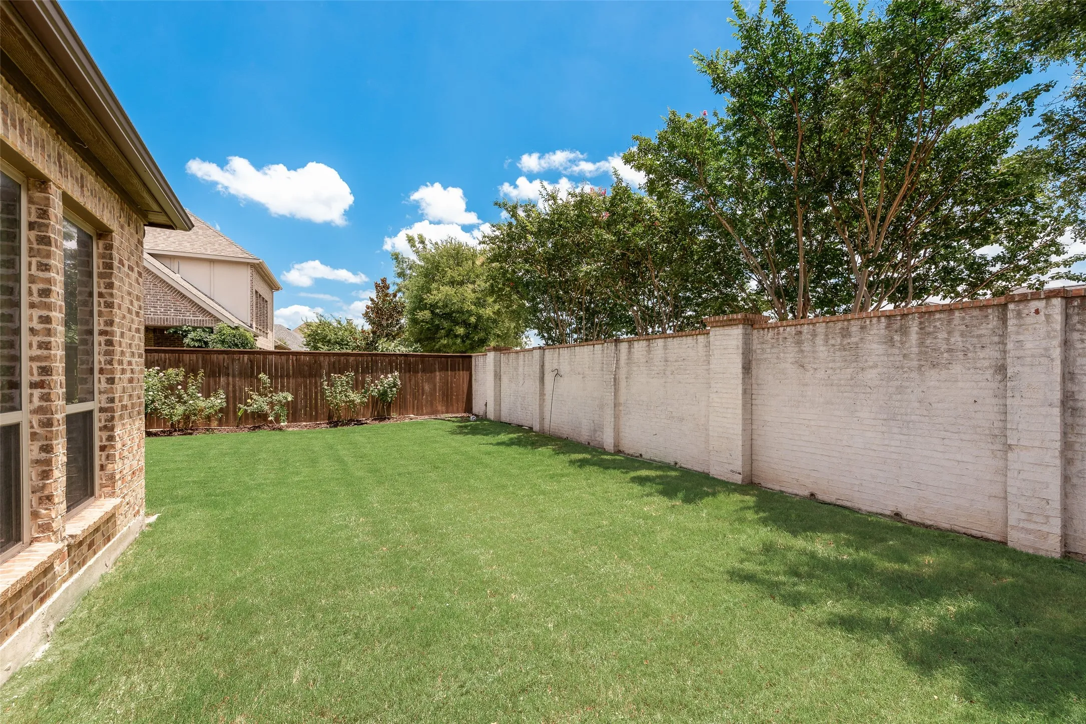 Expansive grass lawn bordered by a brick privacy wall and a wood fence