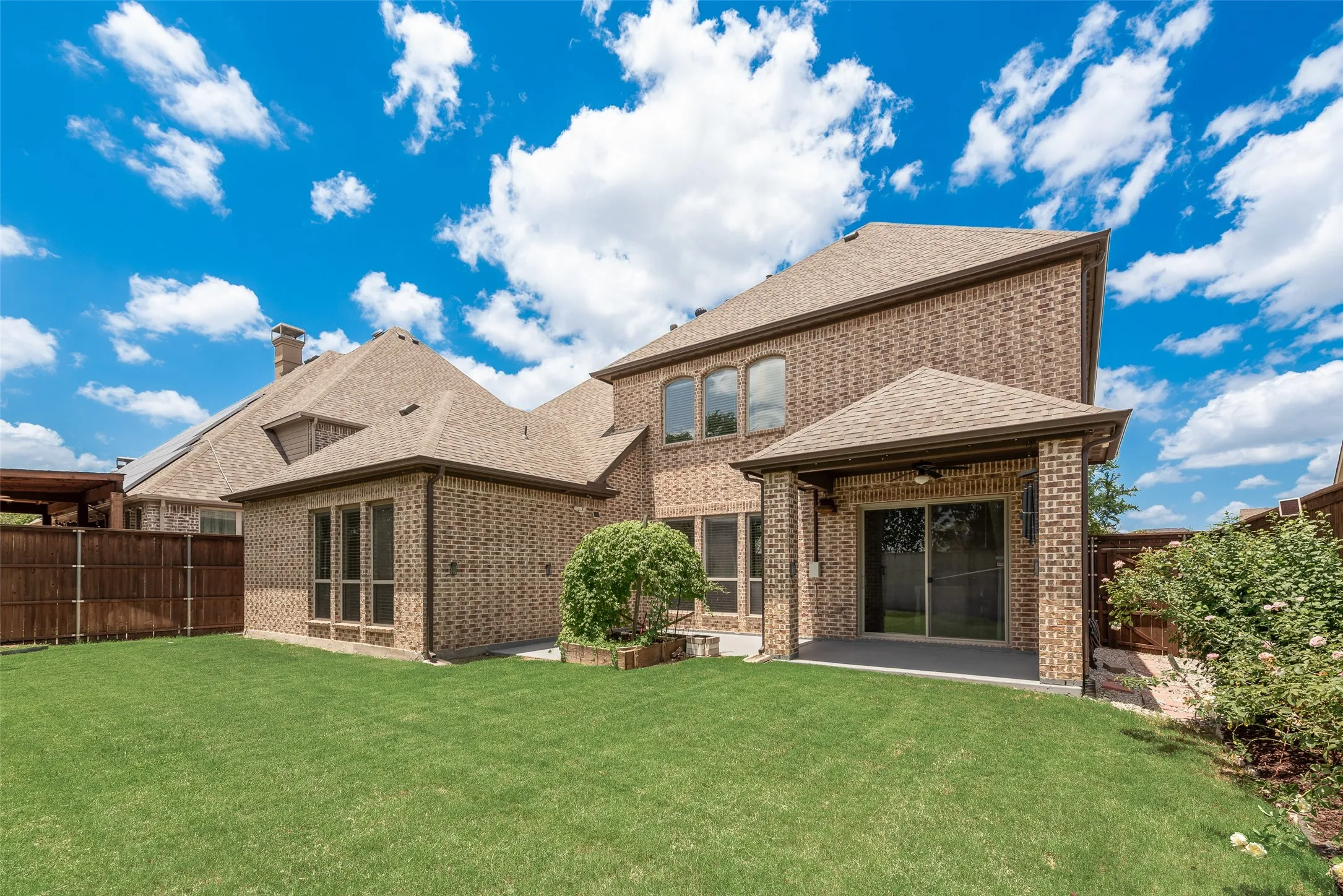 Expansive grassy yard complemented by a brick exterior and covered patio