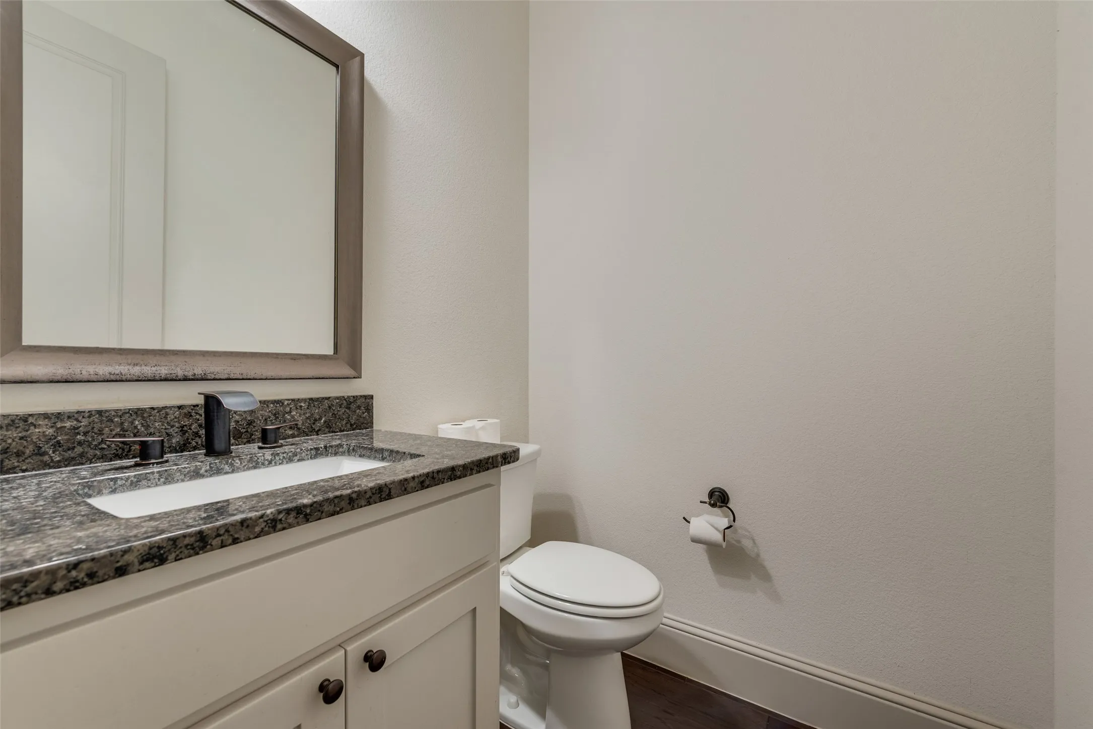 Bathroom vanity with a dark speckled countertop, integrated white sink, and dark bronze faucet