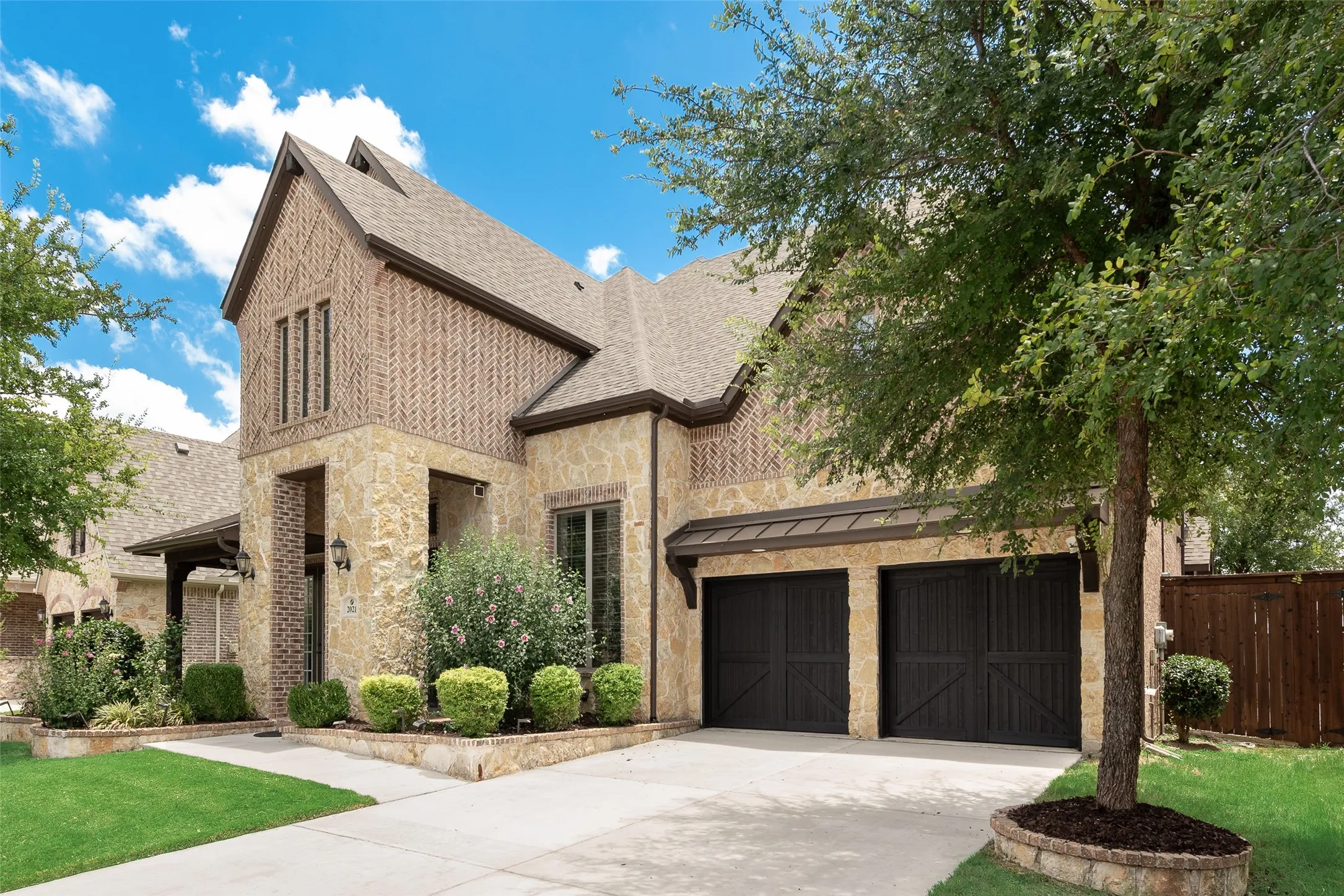 Two-story residence featuring a stone and brick facade, a dual-car garage with dark wood-finish doors, and a concrete driveway