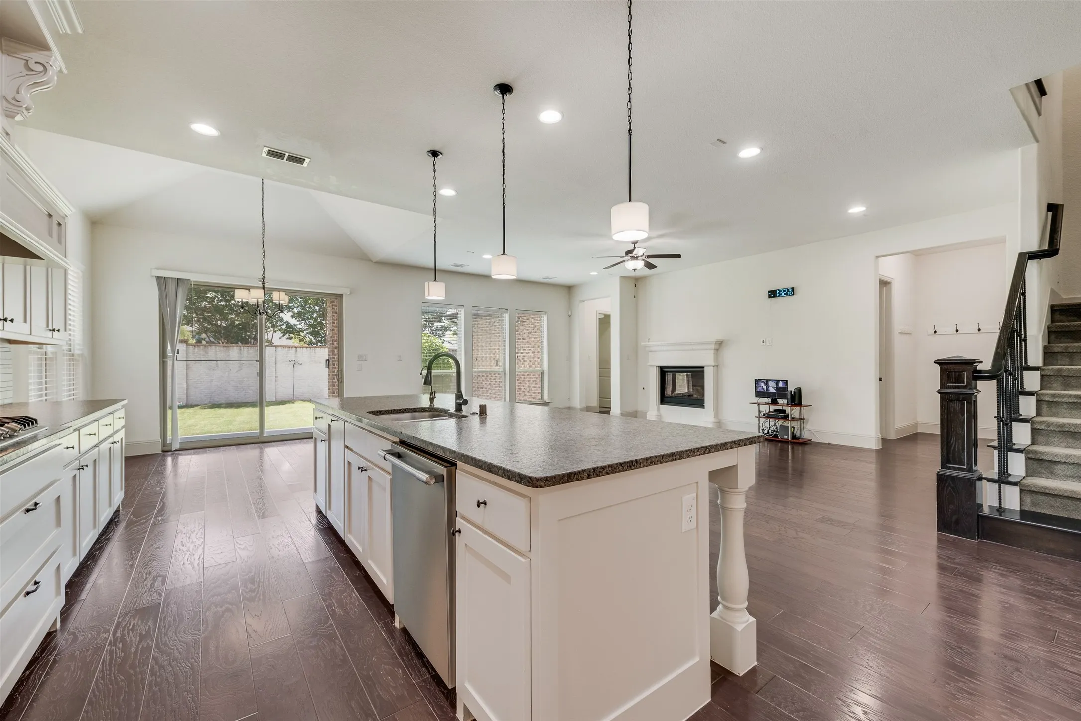 Open-concept living area featuring dark wood-finish flooring, a kitchen island with granite-style countertop, white cabinetry with dark hardware, a built-in fireplace, and a staircase with dark wood newel post and railings