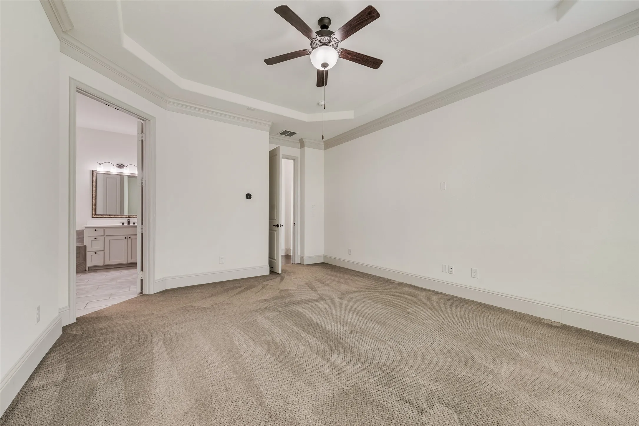 Spacious room featuring tray ceiling, crown molding, gray trim, ceiling fan with integrated lighting, and carpet flooring