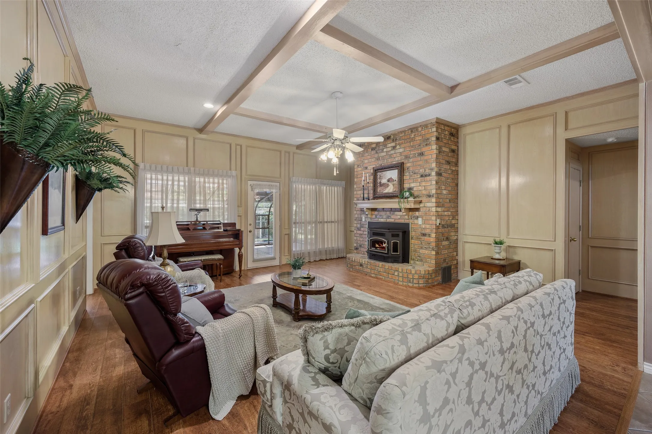 Spacious living area featuring wood-finish flooring, a brick fireplace with a mantel, and decorative paneling on the walls