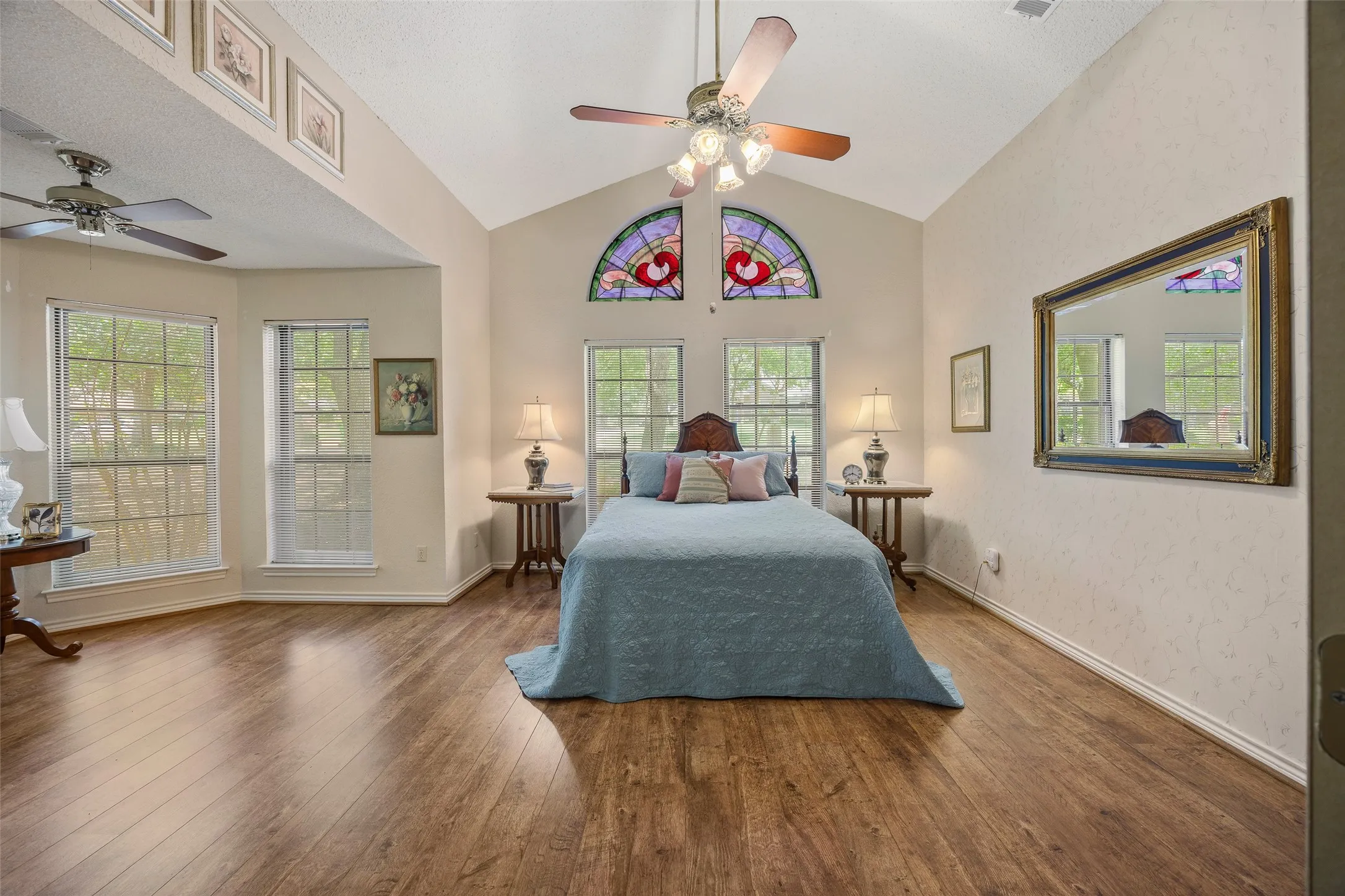 Vaulted ceiling room featuring wood-finish flooring, multiple windows, and decorative stained-glass arch windows