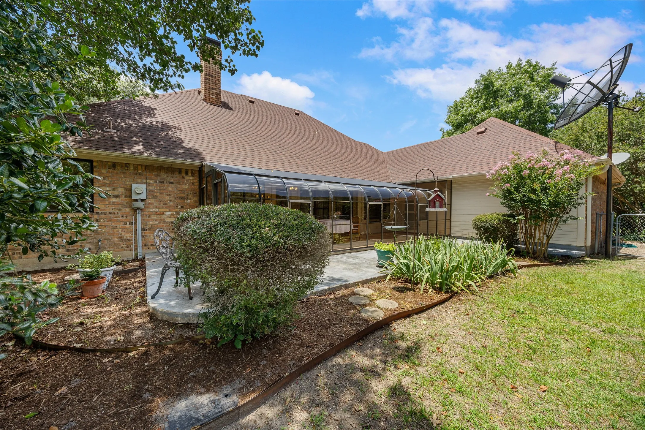 Brick exterior with a sunroom addition and a brown shingle roof