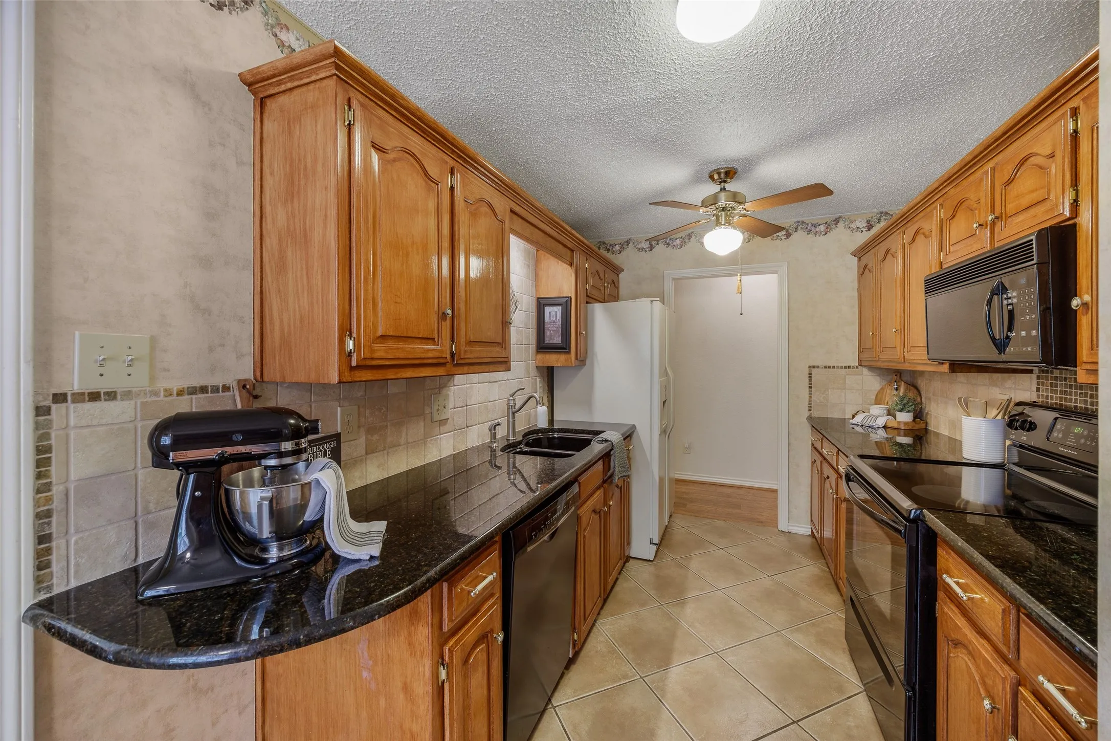 Galley kitchen featuring wood cabinetry, dark countertops, a tile backsplash, and tile flooring