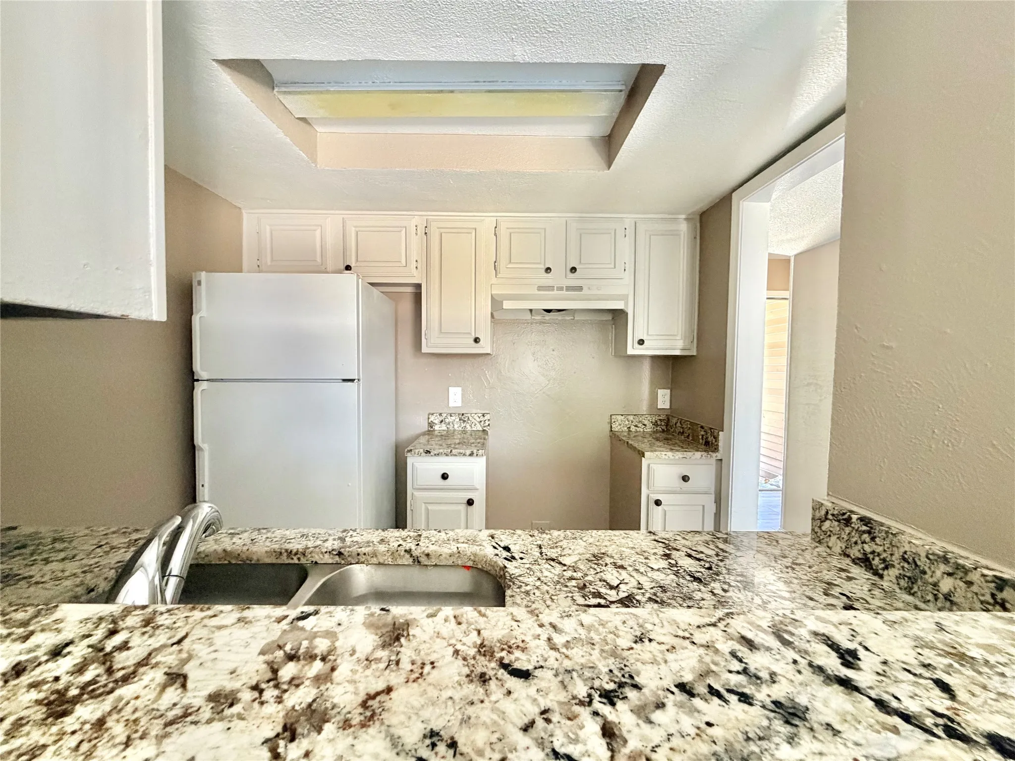 Kitchen featuring white cabinetry, granite-style countertops, an undermount double-basin stainless steel sink with a chrome faucet, and a built-in overhead light fixture