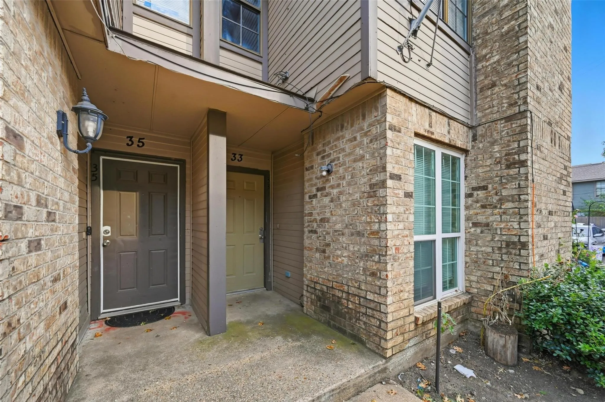 Brick exterior featuring an entry door with an overhead light fixture, a sidelight window, and a concrete landing