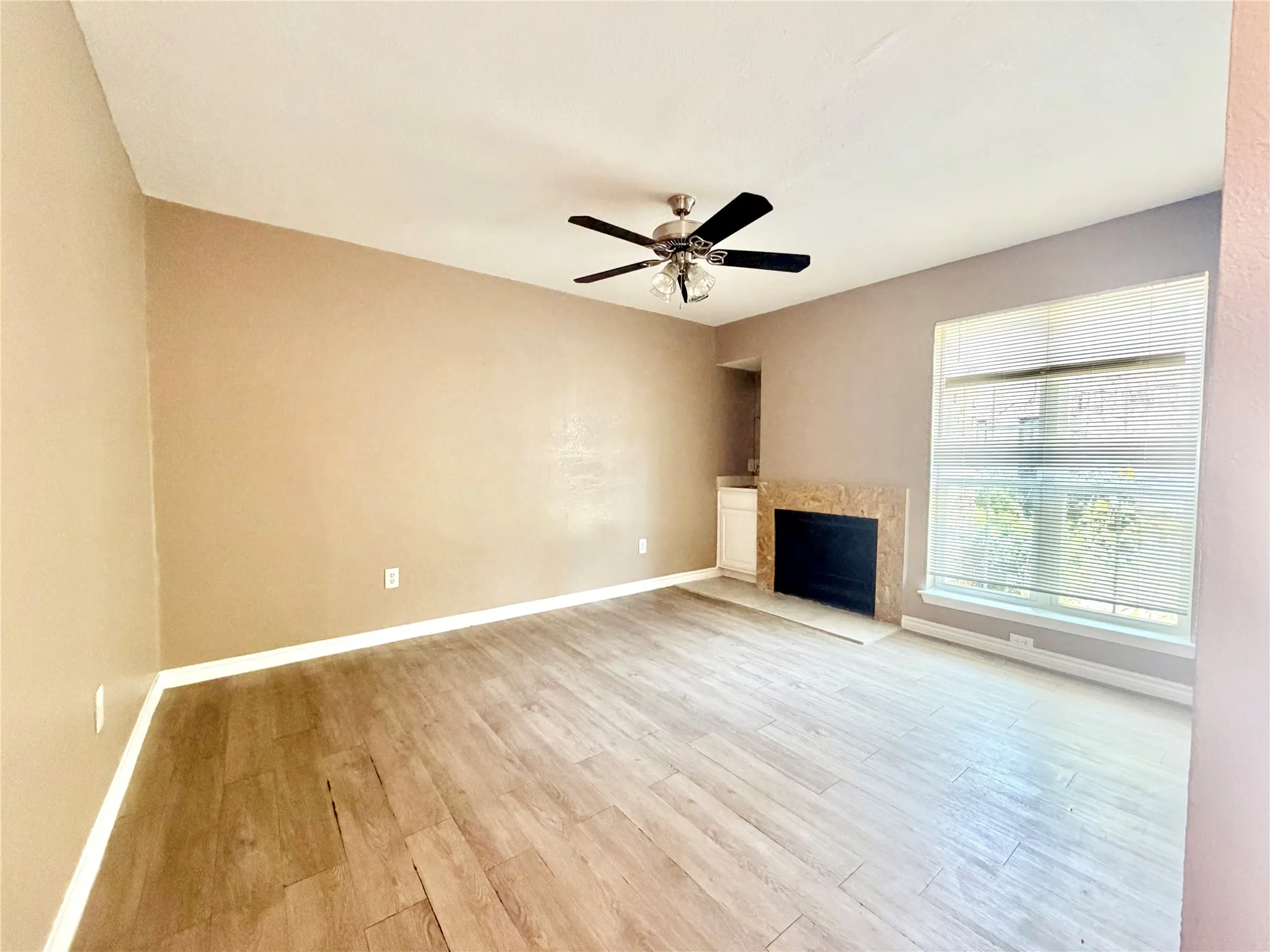 Spacious room featuring wood-finish flooring, a ceiling fan, and a fireplace with a stone surround