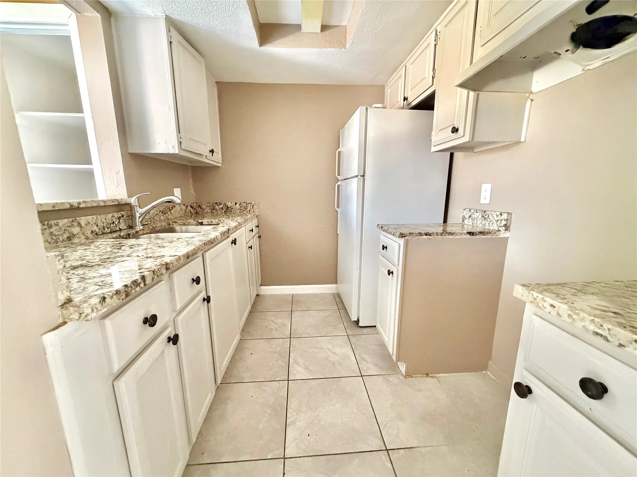 Kitchen featuring light-toned cabinetry with dark hardware, granite-style countertops, an undermount sink, and tiled flooring