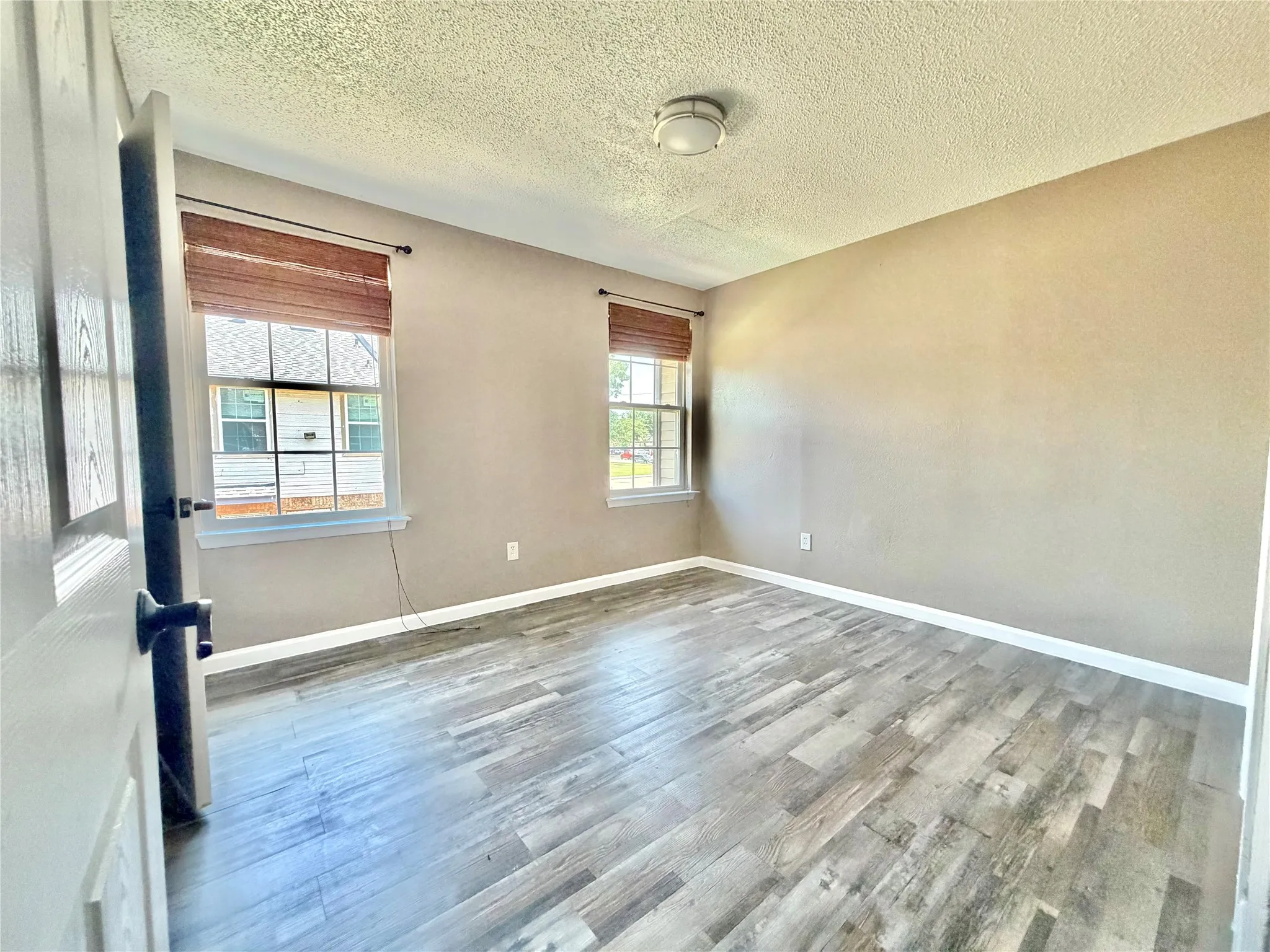 Room featuring wood-finish flooring, two large windows with woven blinds, and neutral wall tones