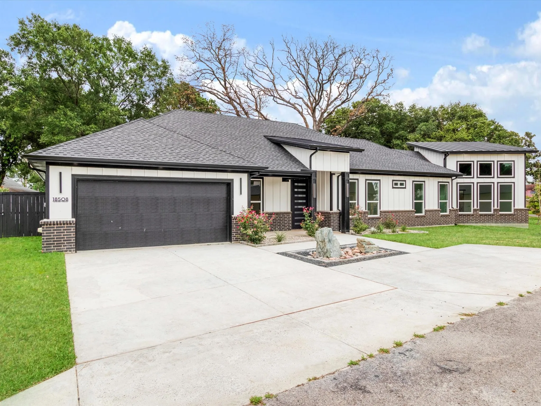 Contemporary exterior featuring white vertical siding, dark brick accents, a black roof, a black garage door, and a concrete driveway