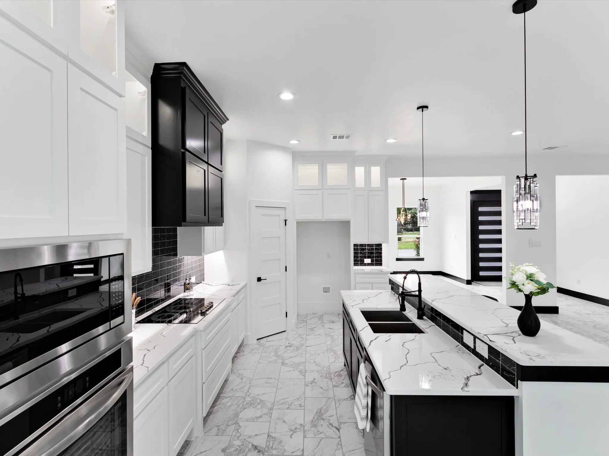 Modern kitchen featuring an expansive center island with dual sinks, white countertops, black cabinetry, and stainless steel appliances