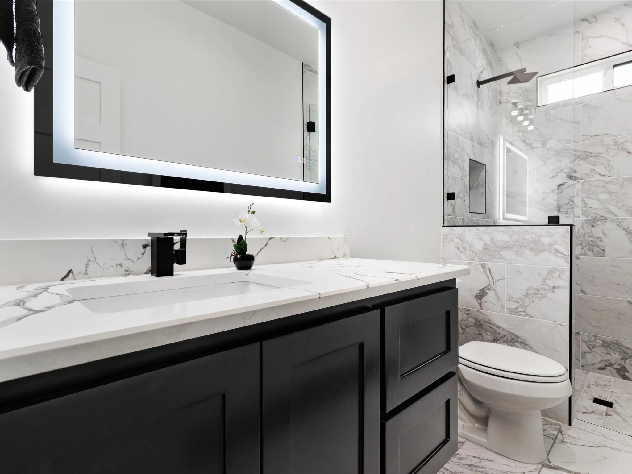 Modern bathroom featuring a dark vanity with panel-front cabinetry, a white countertop with integrated sink, and a black faucet