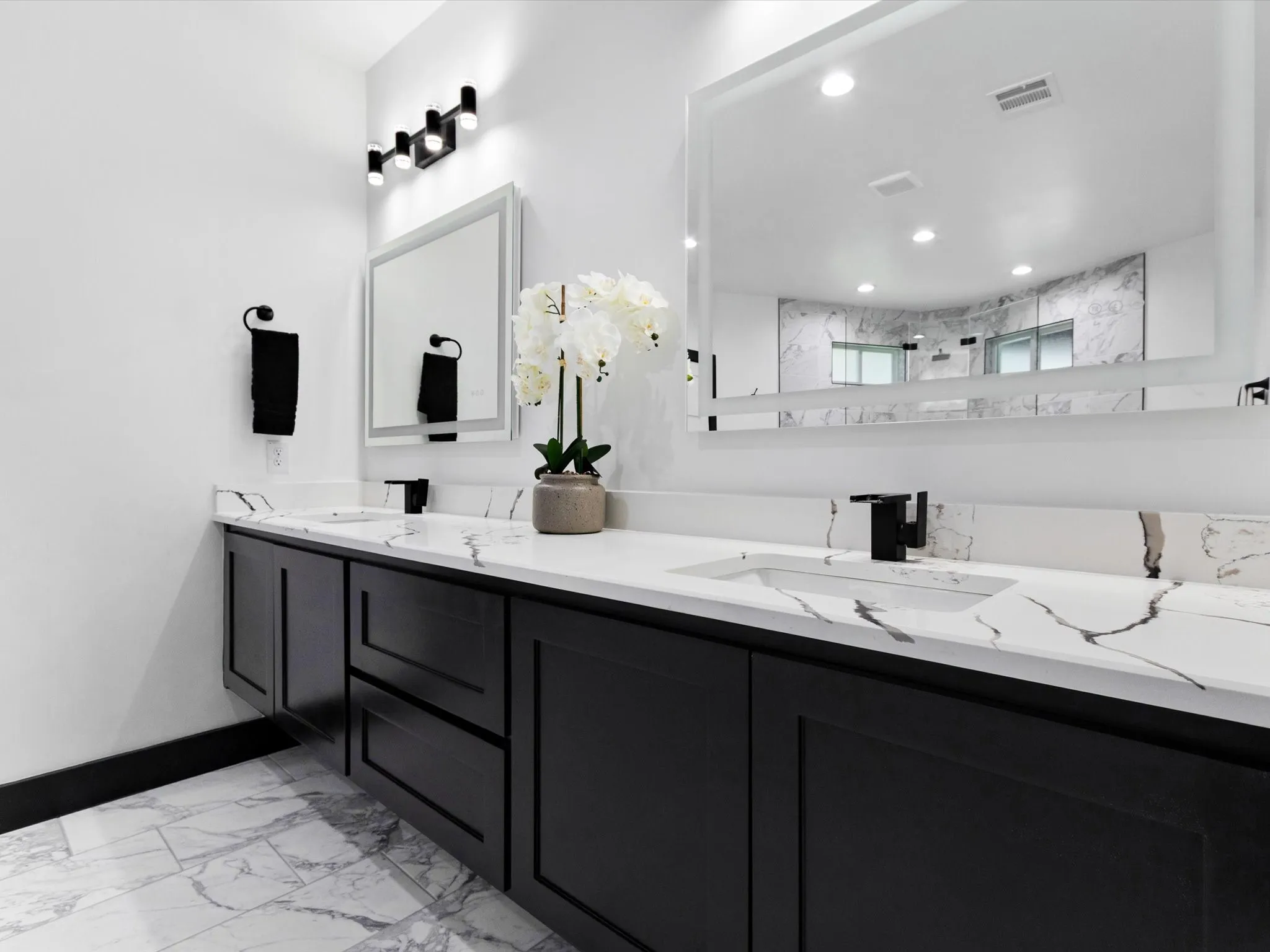 Dual vanity featuring black shaker-style cabinetry, white countertops with prominent veining, and integrated sinks with matte black fixtures
