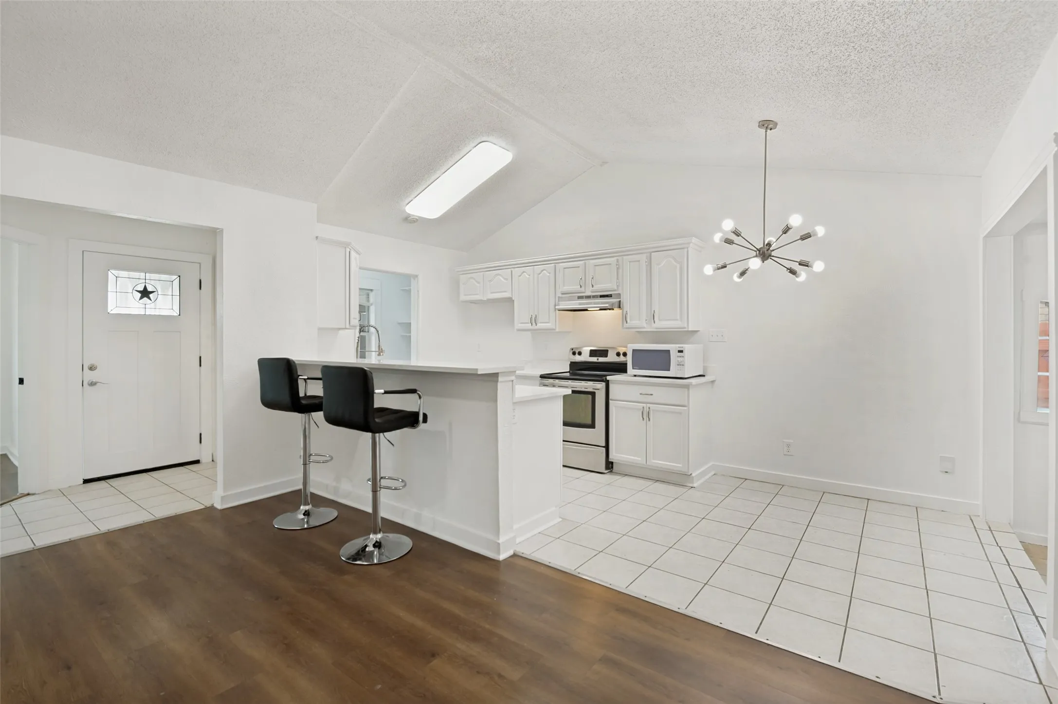 Open concept living area featuring a breakfast bar with seating, white kitchen cabinetry, stainless steel appliances, and a modern sputnik chandelier