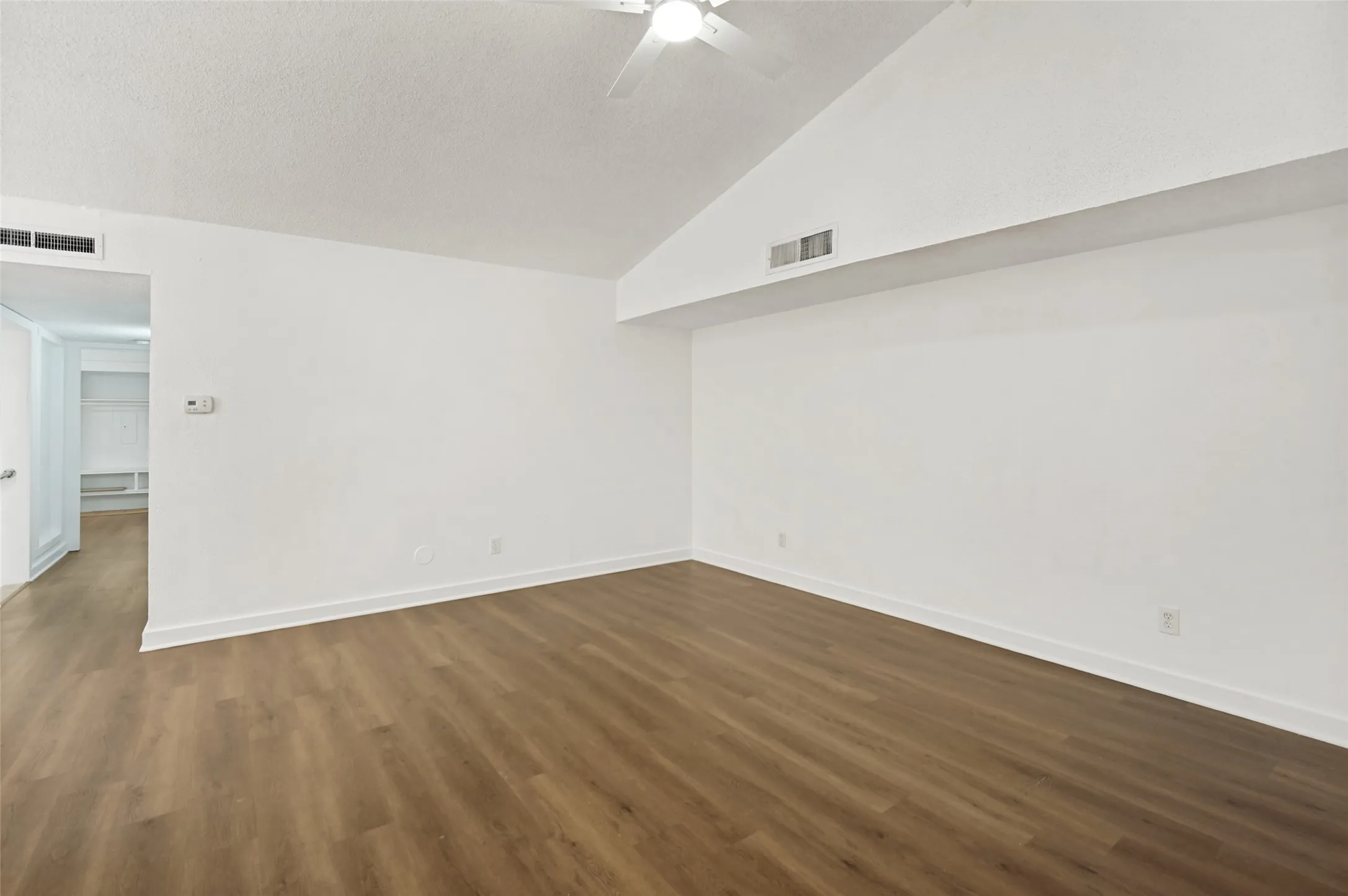 Spacious room featuring vaulted ceilings, wood-finish flooring, crisp white walls, and a ceiling fan
