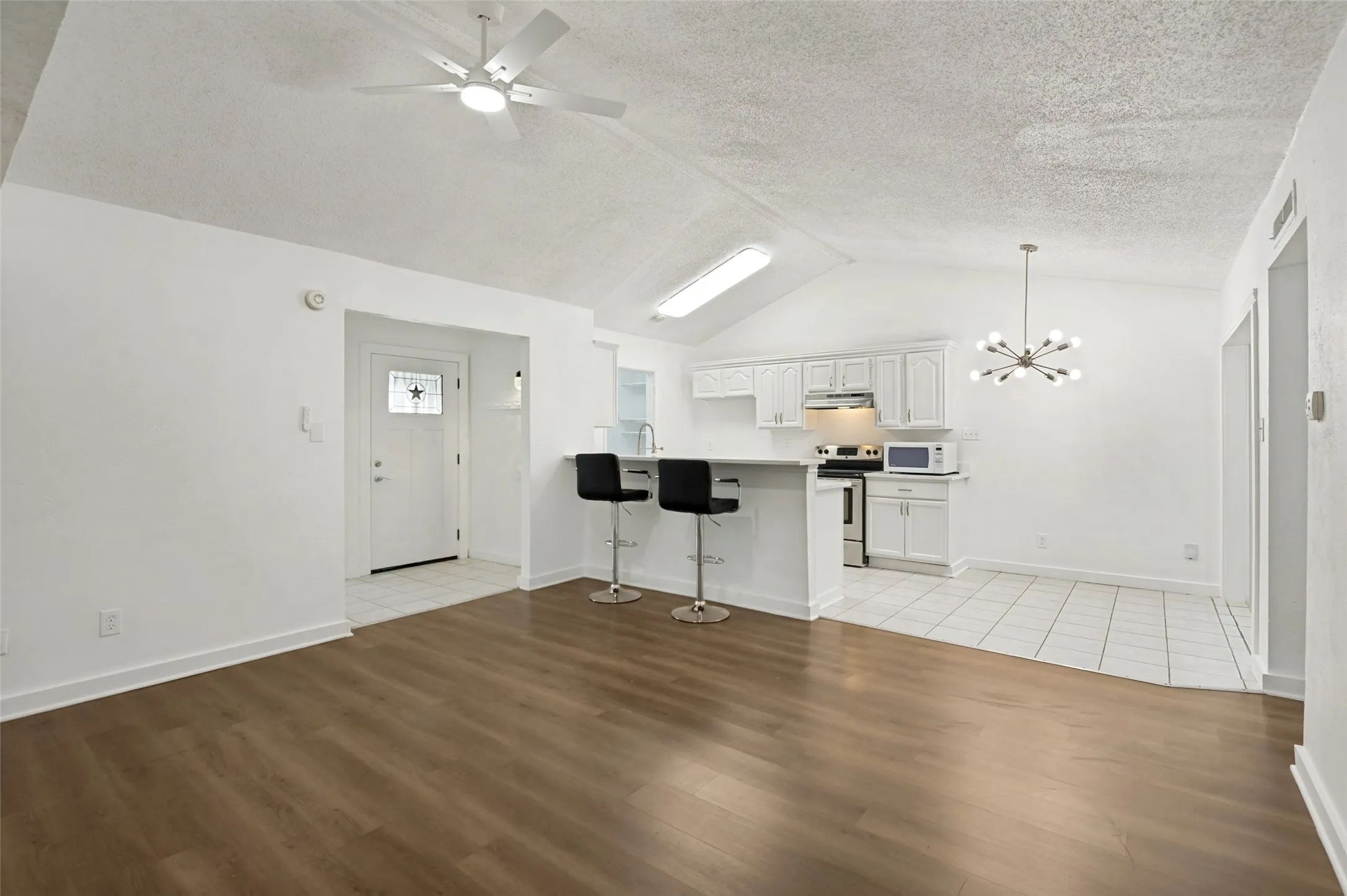 Open-concept living area featuring wood-finish flooring, vaulted ceiling, and an updated kitchen with white cabinetry and a breakfast bar