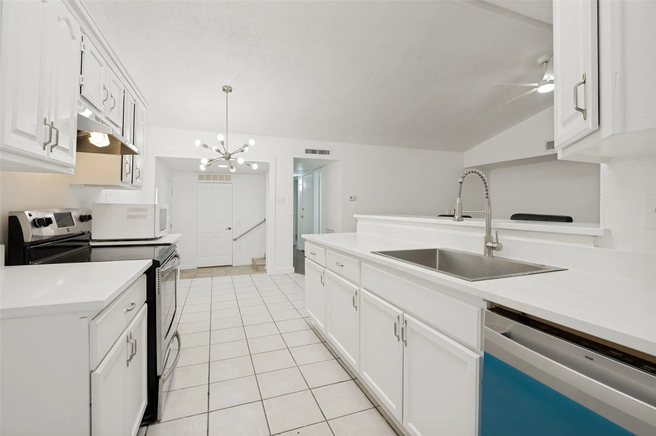 Bright kitchen featuring white cabinetry, white countertops, tile flooring, and a modern sputnik chandelier