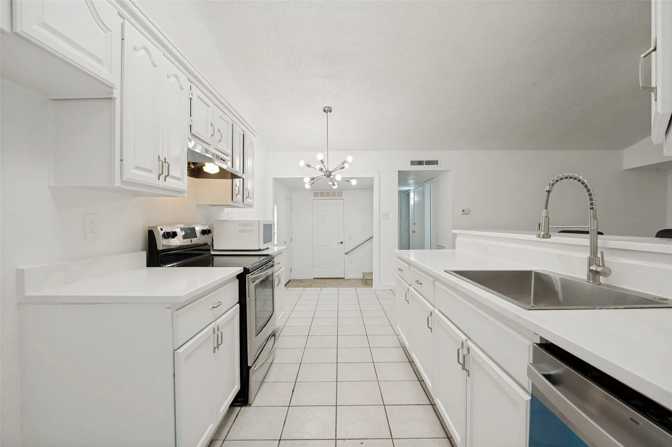Galley kitchen featuring white cabinetry, light countertops, stainless steel appliances, a double basin sink with a pull-down faucet, and tiled flooring
