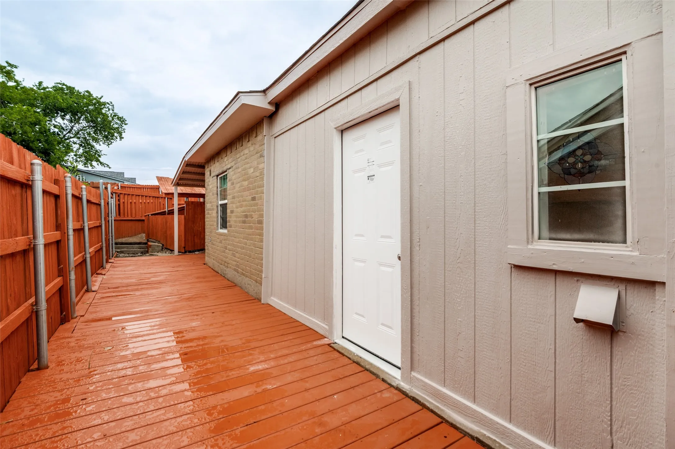Exterior walkway featuring a wood-finish deck, privacy fencing, and a white paneled door