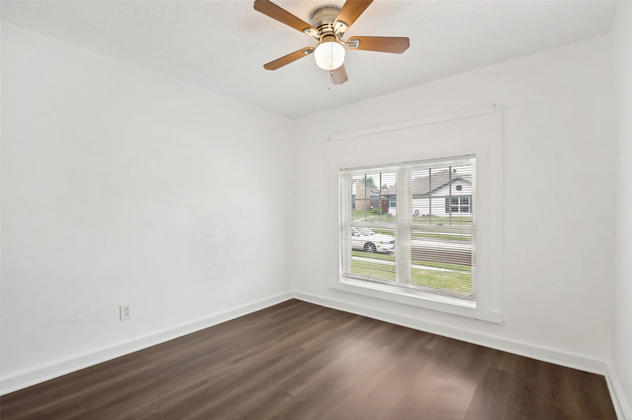 Bright room featuring wood-finish flooring, white walls, and a ceiling fan with integrated lighting