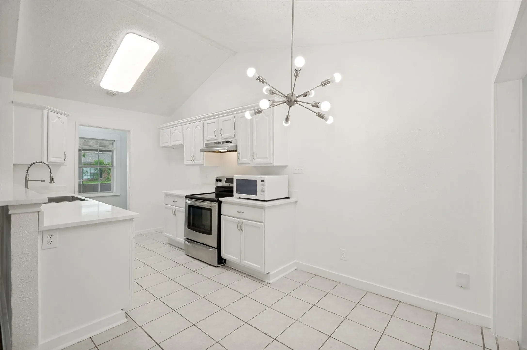 Kitchen featuring white cabinetry, stainless steel appliances, a vaulted ceiling, and tile flooring