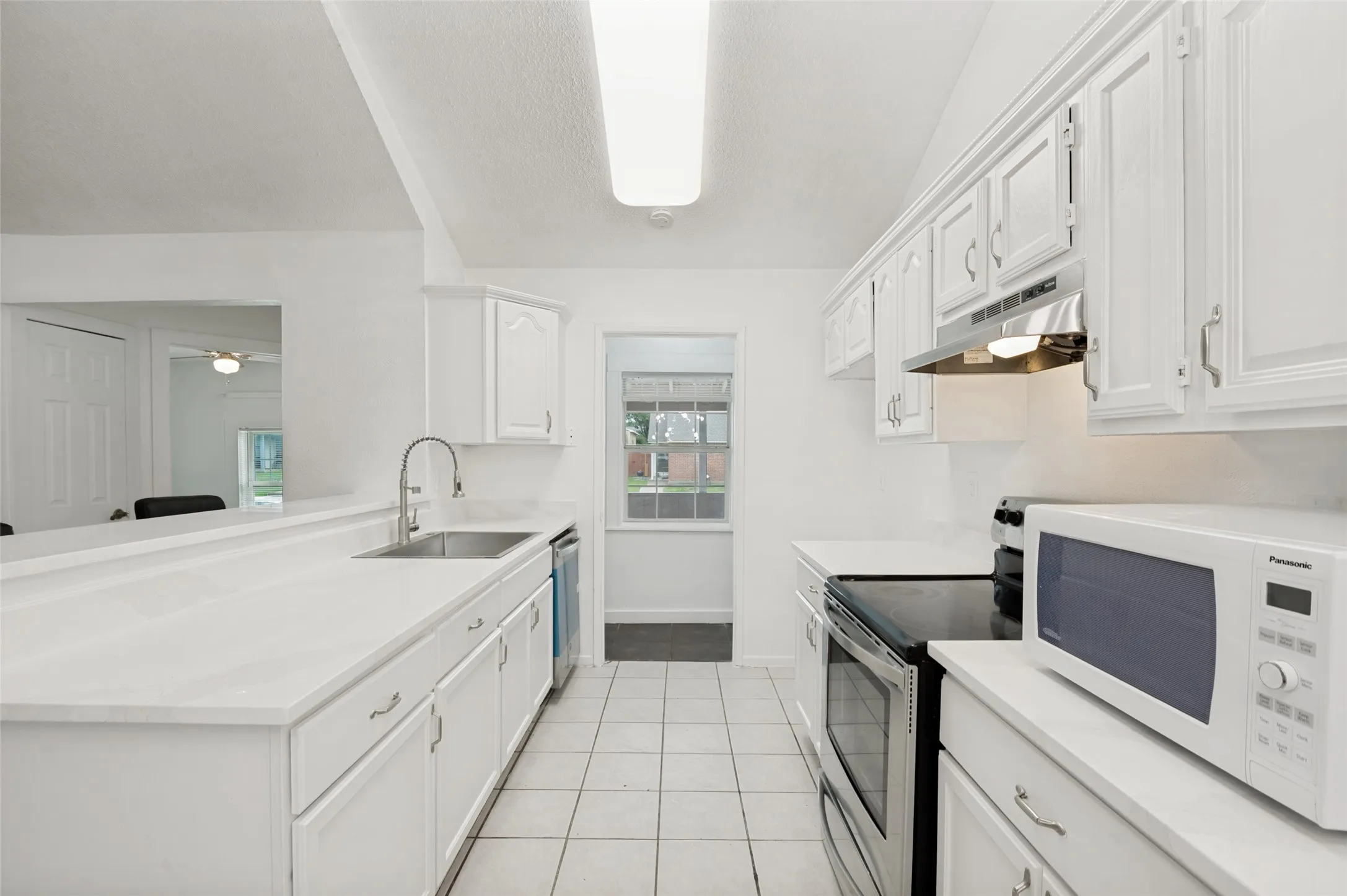 Updated kitchen featuring white cabinetry, light-toned countertops, stainless steel appliances, and tile flooring