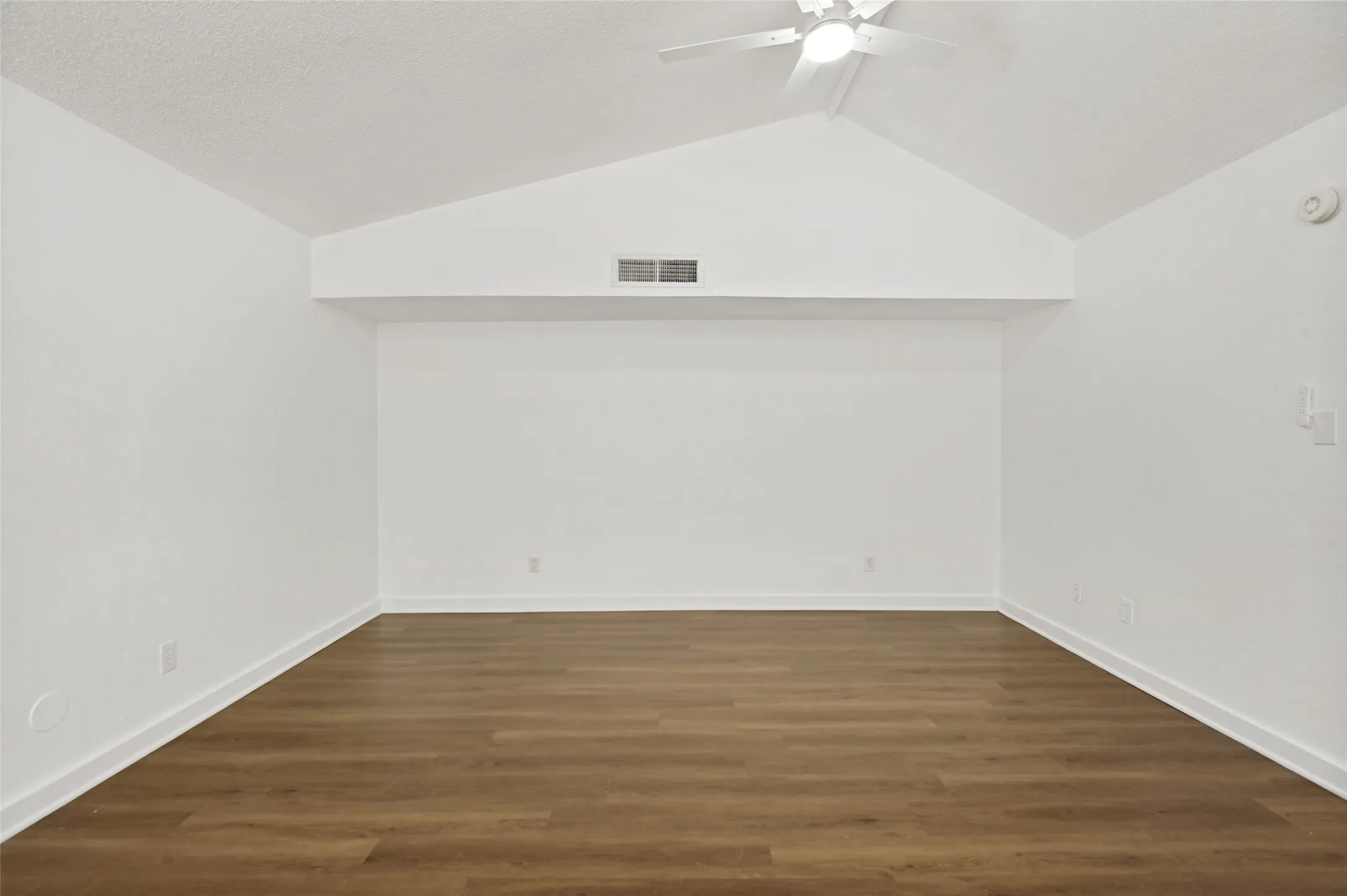 Spacious room featuring vaulted ceilings, a ceiling fan, wood-finish flooring, and crisp white walls
