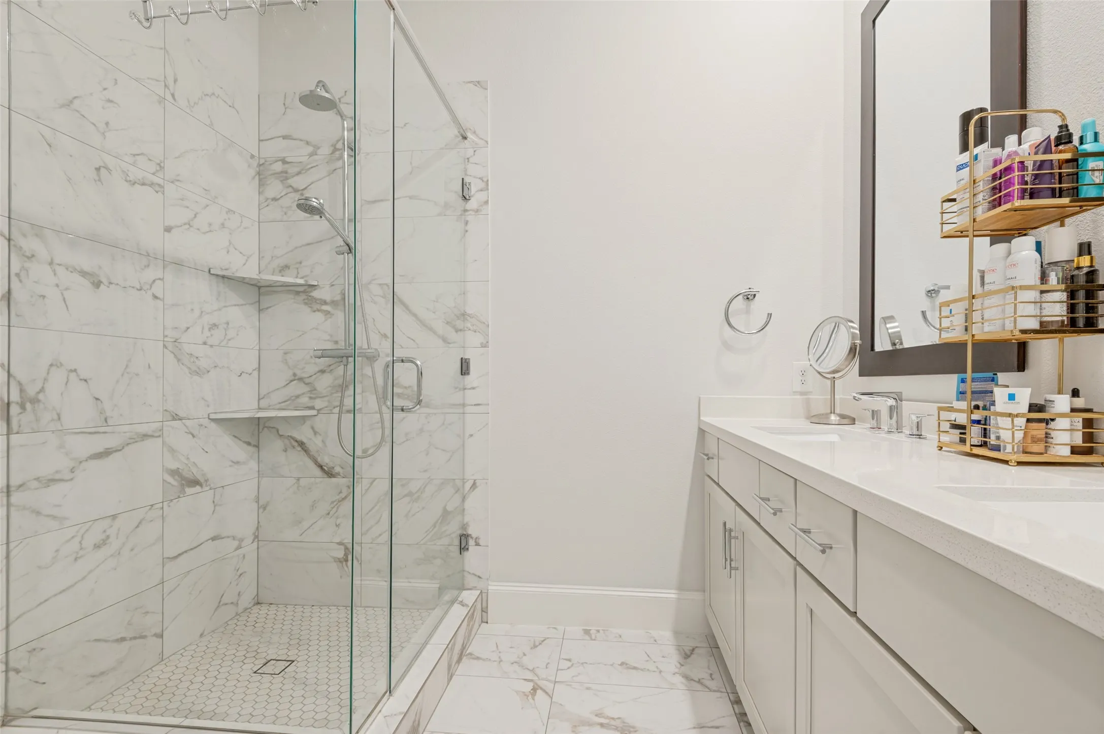 Spacious bathroom featuring a glass-enclosed shower with large format marble-look tile walls, dual shower heads, and built-in shelving