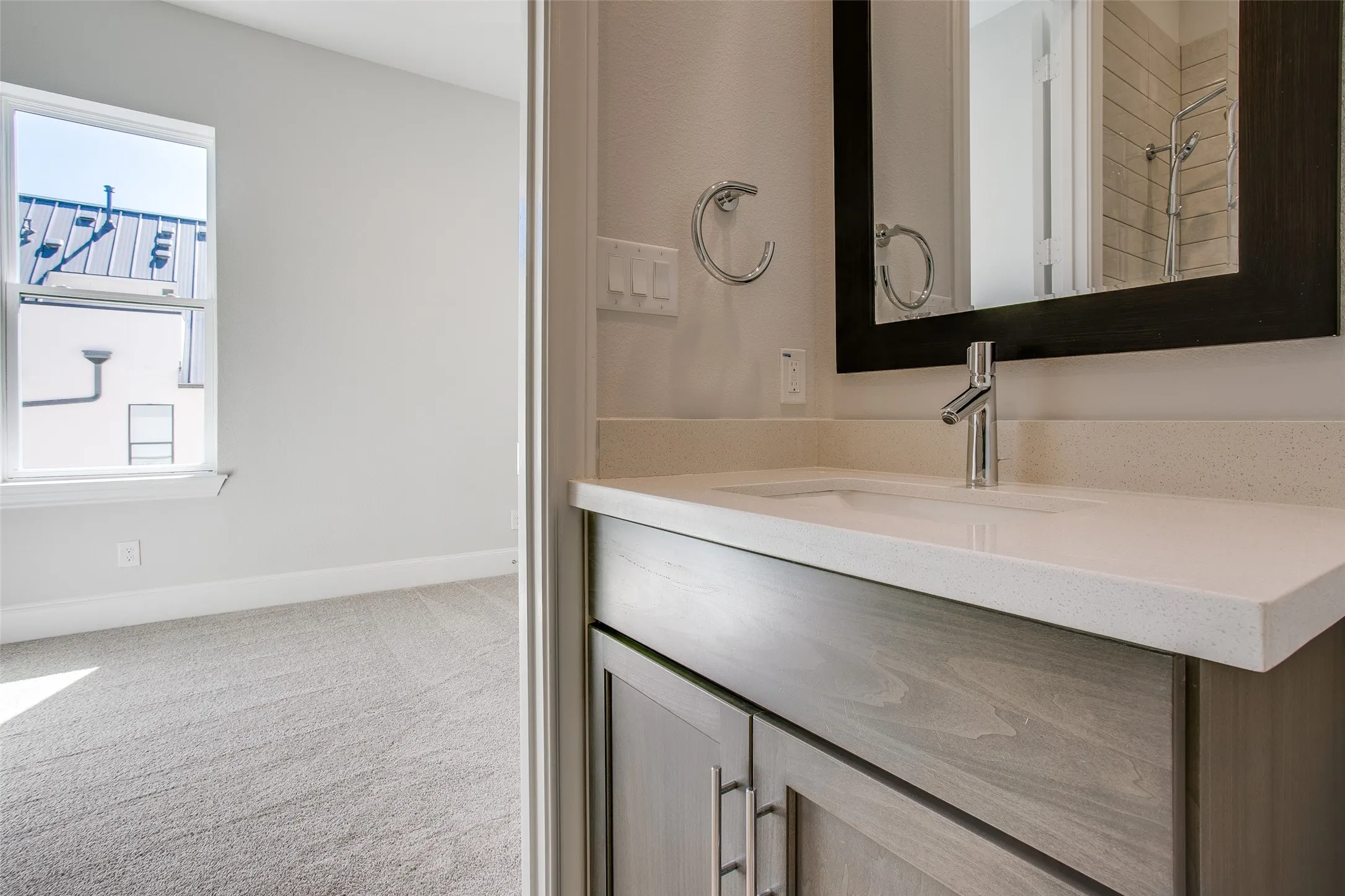 Bathroom vanity featuring a light-toned countertop with an integrated sink, chrome faucet, and a dark-framed mirror