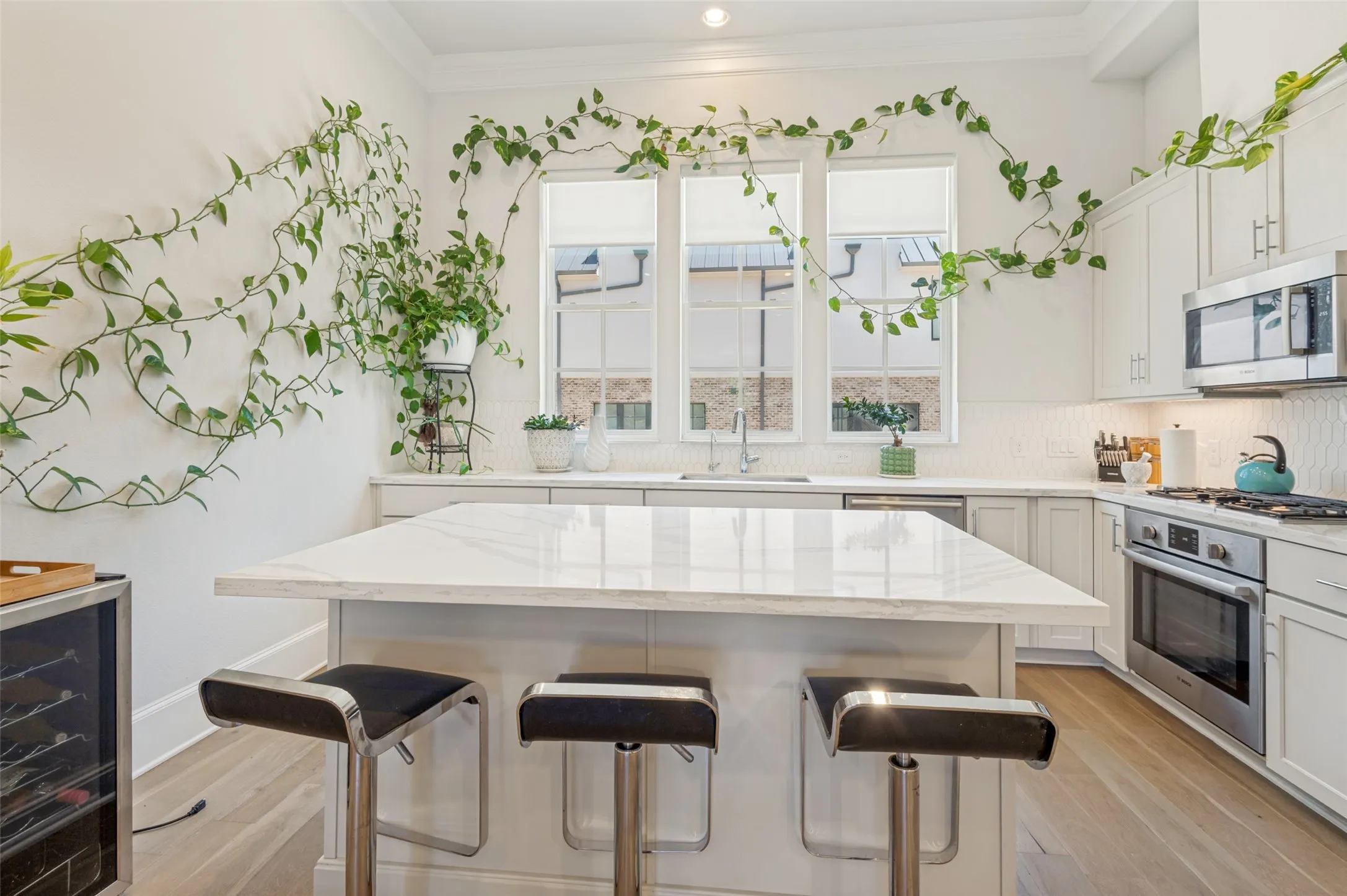 Bright kitchen featuring a central island with a stone countertop, white shaker cabinetry, stainless steel appliances, and wood-finish flooring