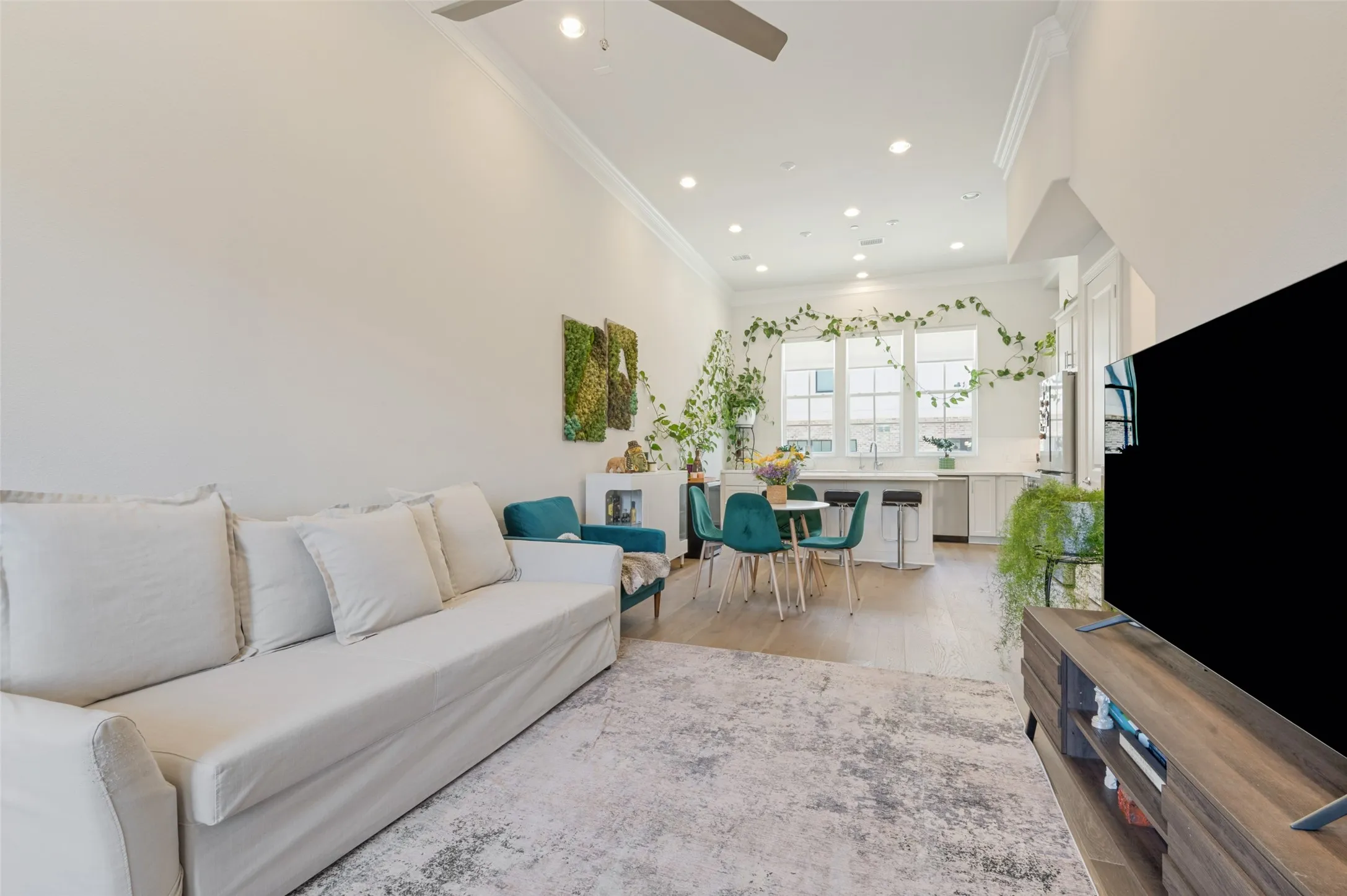 Open-concept living space featuring high ceilings, crown molding, wood-finish flooring, recessed lighting, and a kitchen with white cabinetry and a breakfast bar