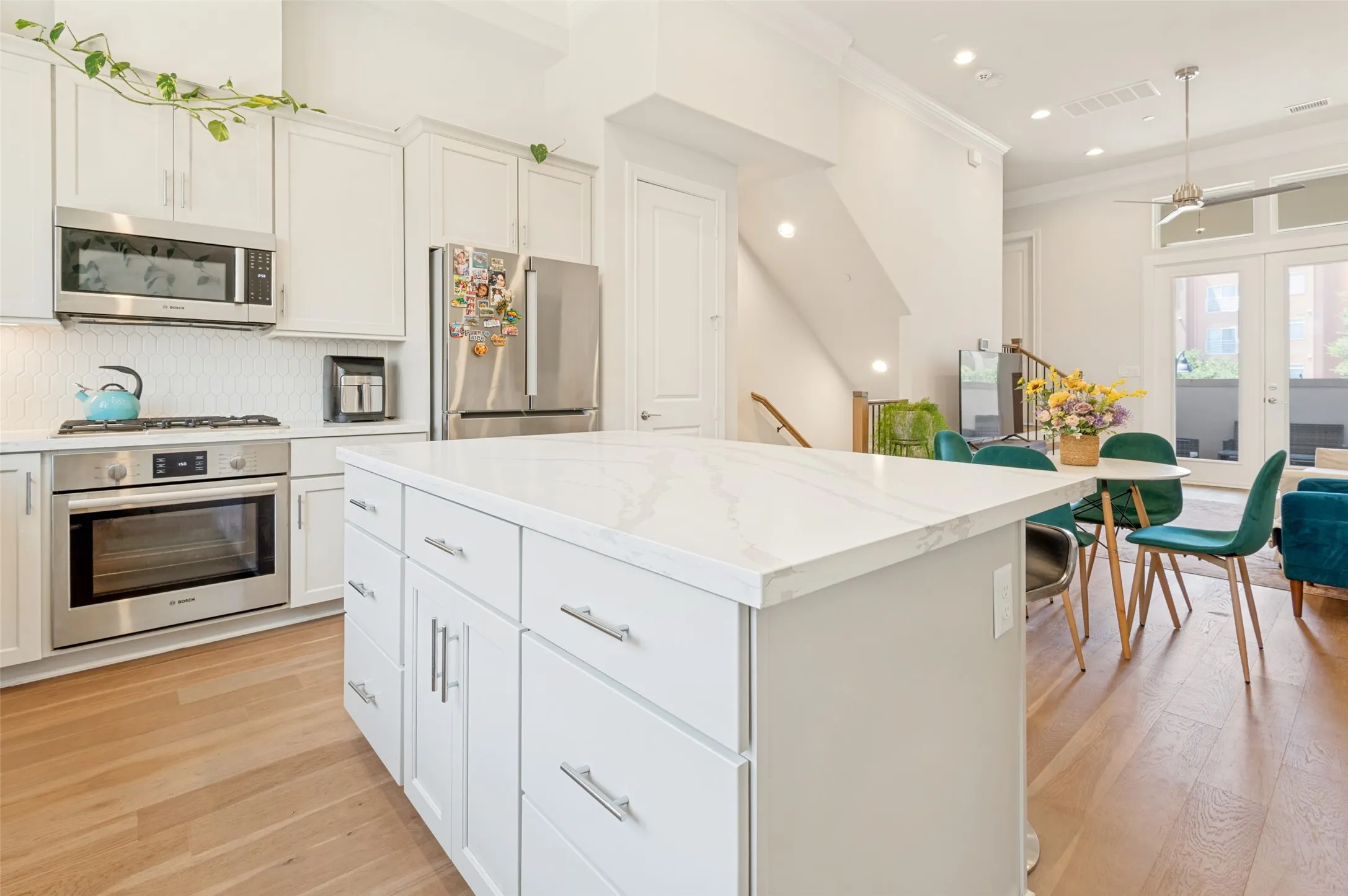 Gourmet kitchen with a large central island featuring a light-colored countertop, white shaker-style cabinetry, stainless steel appliances, and wood-finish flooring