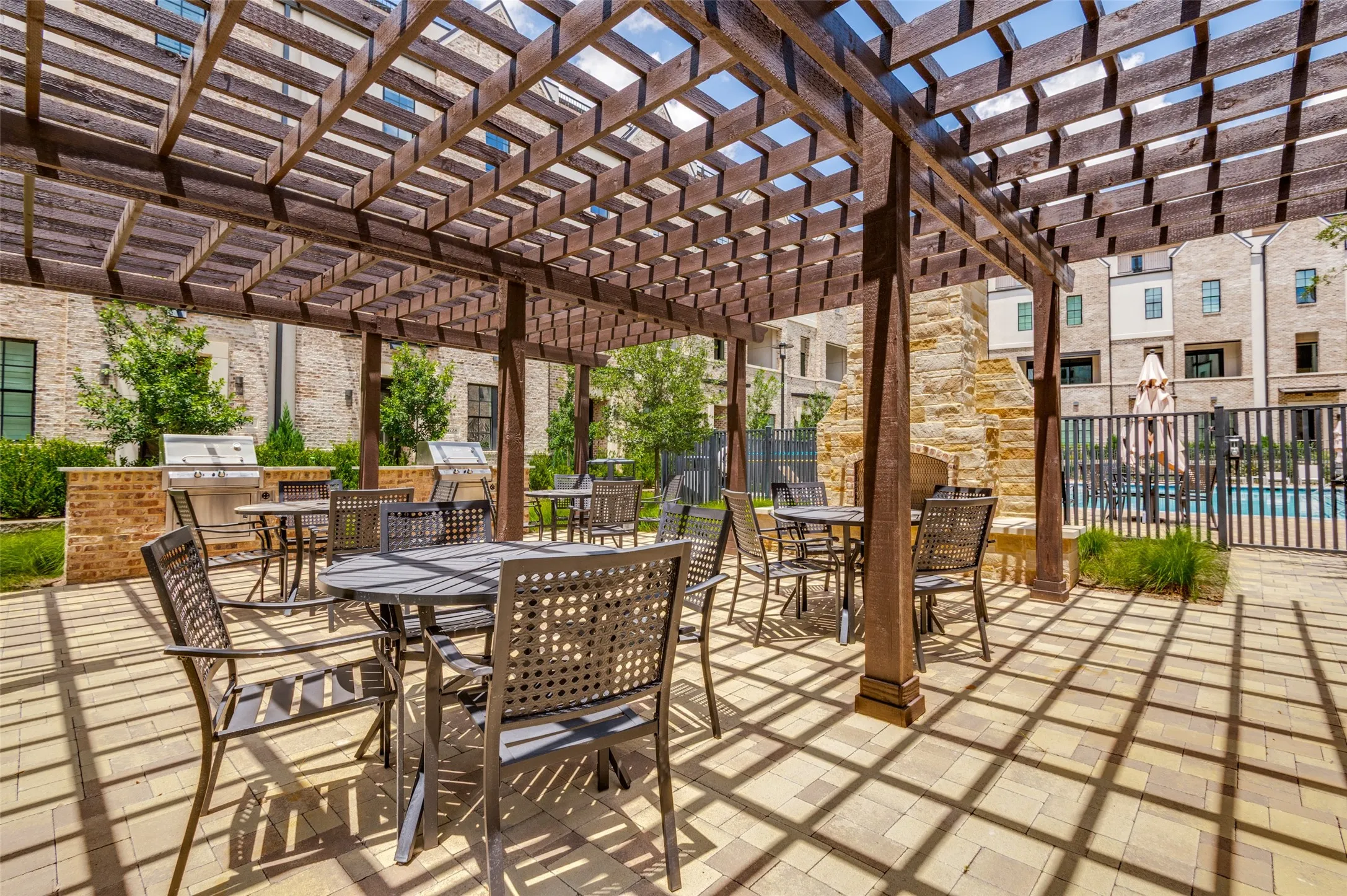 Outdoor entertaining area featuring a large wooden pergola, paver flooring, multiple dining tables, and built-in grilling stations with brick surrounds