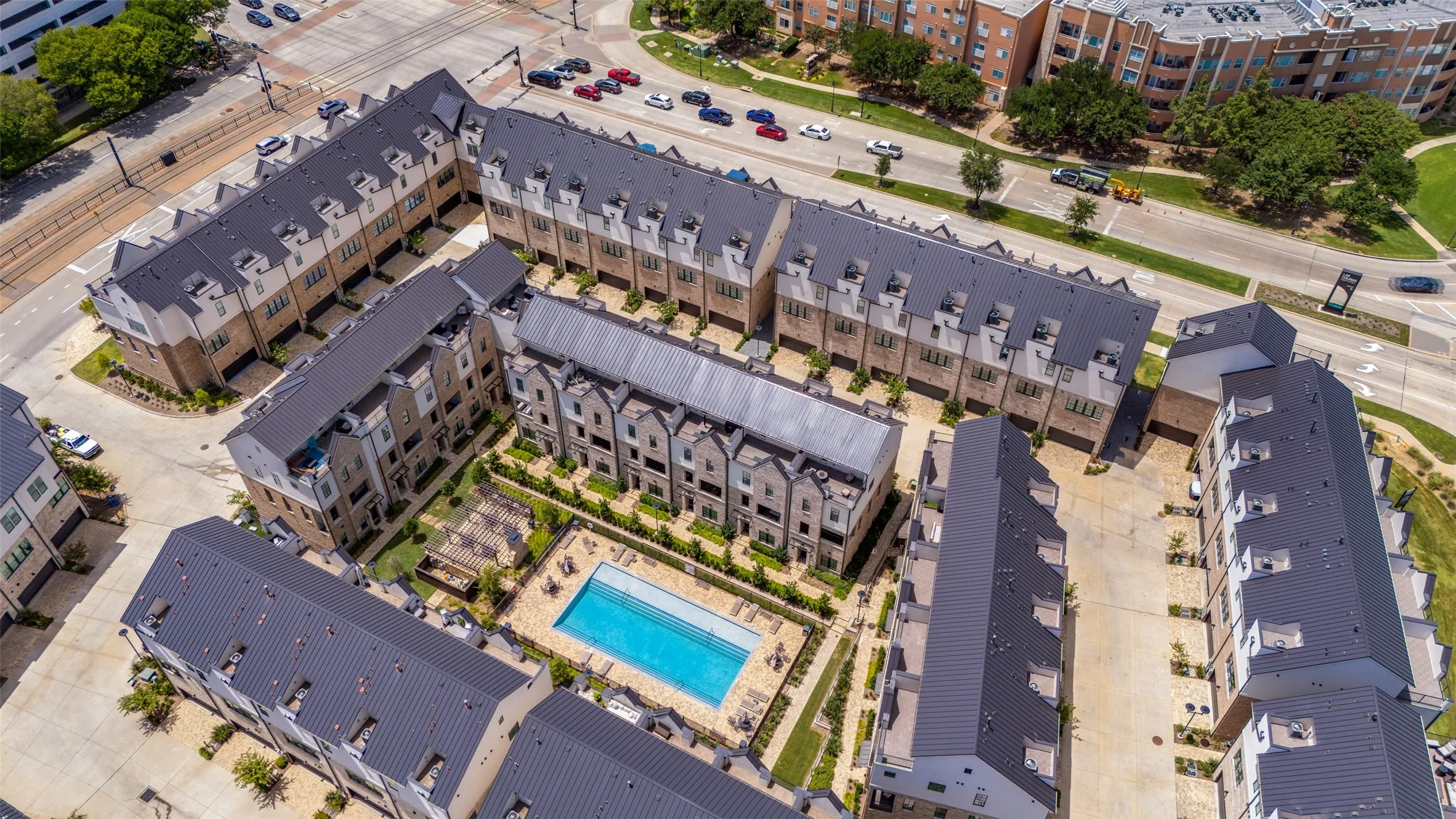 Aerial view of a contemporary multi-story residential complex featuring dark metal roofs, light-colored facades, multiple dormer windows, and a central courtyard with an in-ground swimming pool