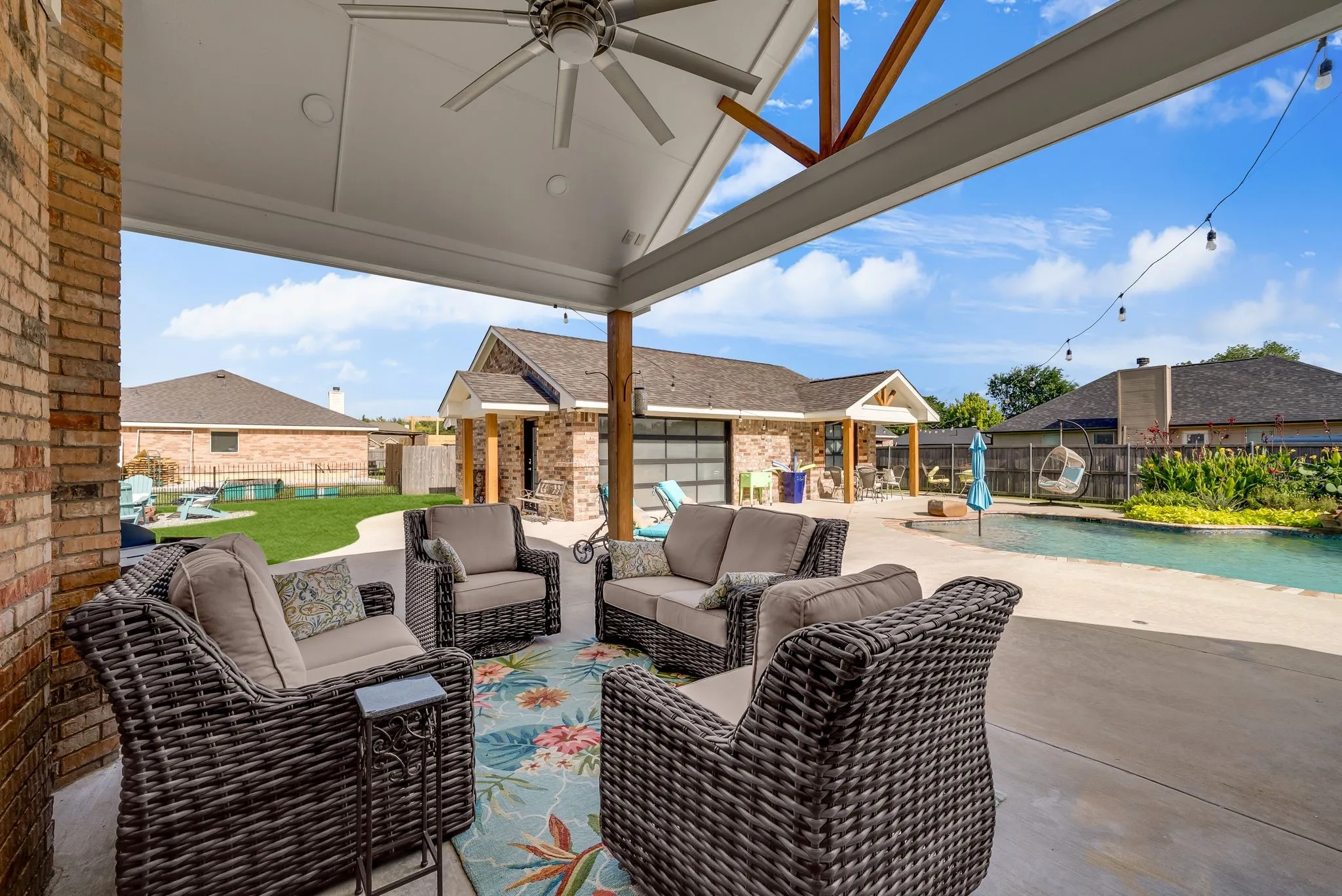Covered patio featuring a ceiling fan, exposed wood beams, brick facade, and concrete flooring