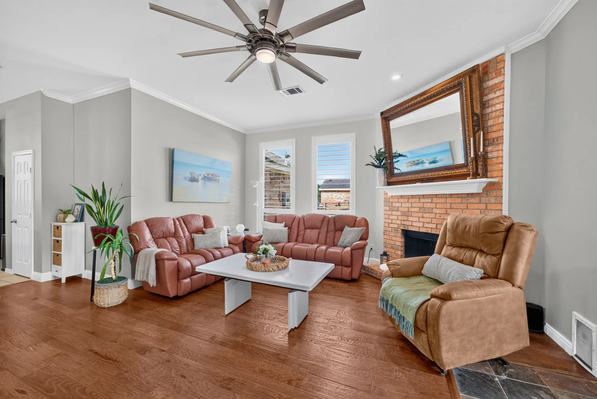 Living area featuring wood-finish flooring, a brick fireplace with a white mantel, and crown molding
