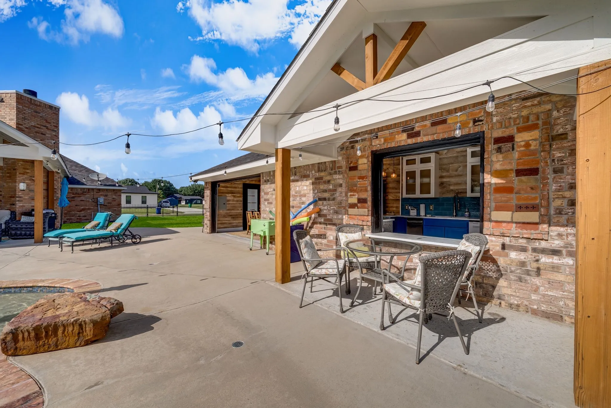 Spacious concrete patio featuring a brick exterior with a pass-through window, wood support beams, and exposed rafter tails