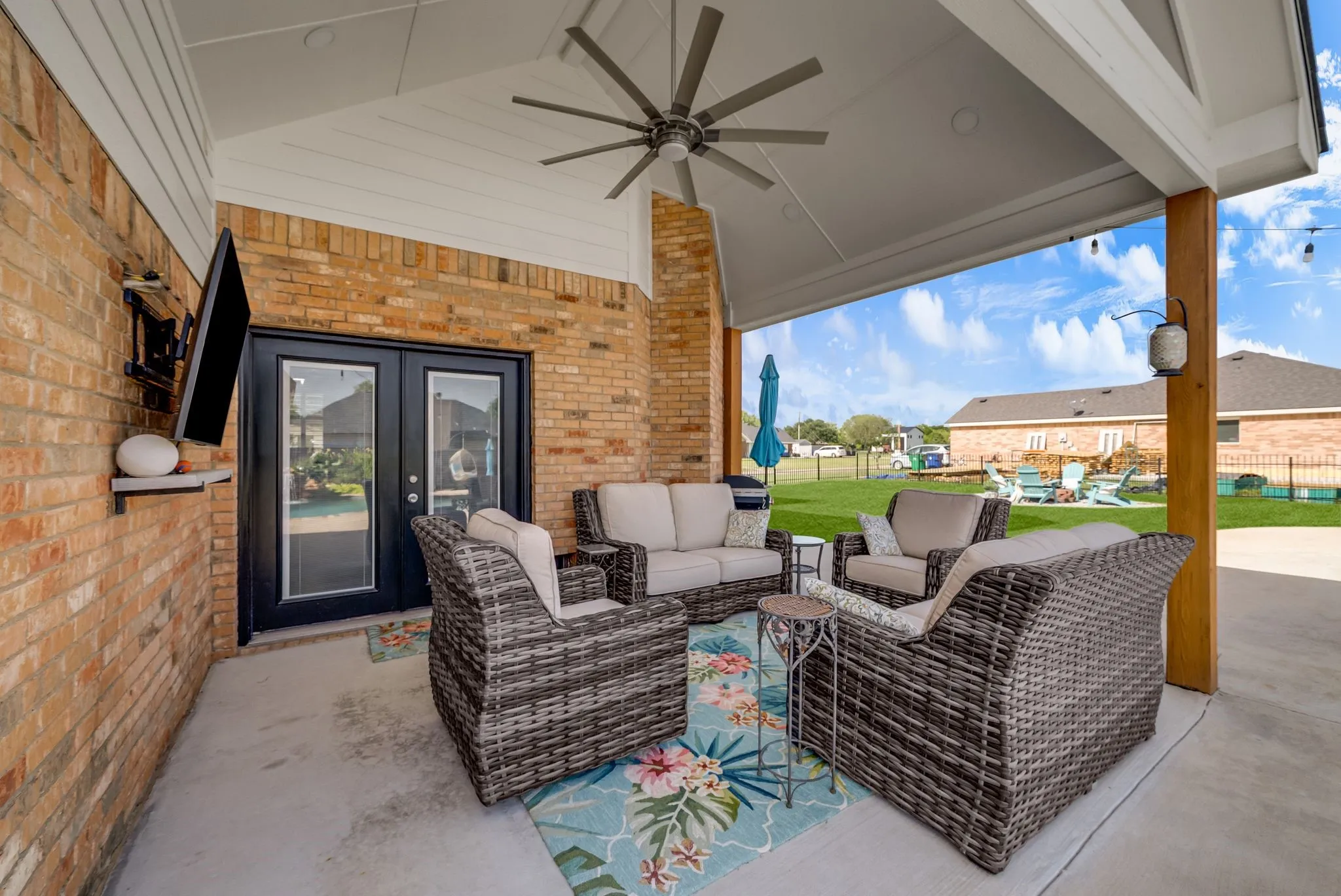 Expansive covered patio featuring a vaulted ceiling with a large ceiling fan, string lights, a brick exterior wall, and direct access to the interior via double glass doors