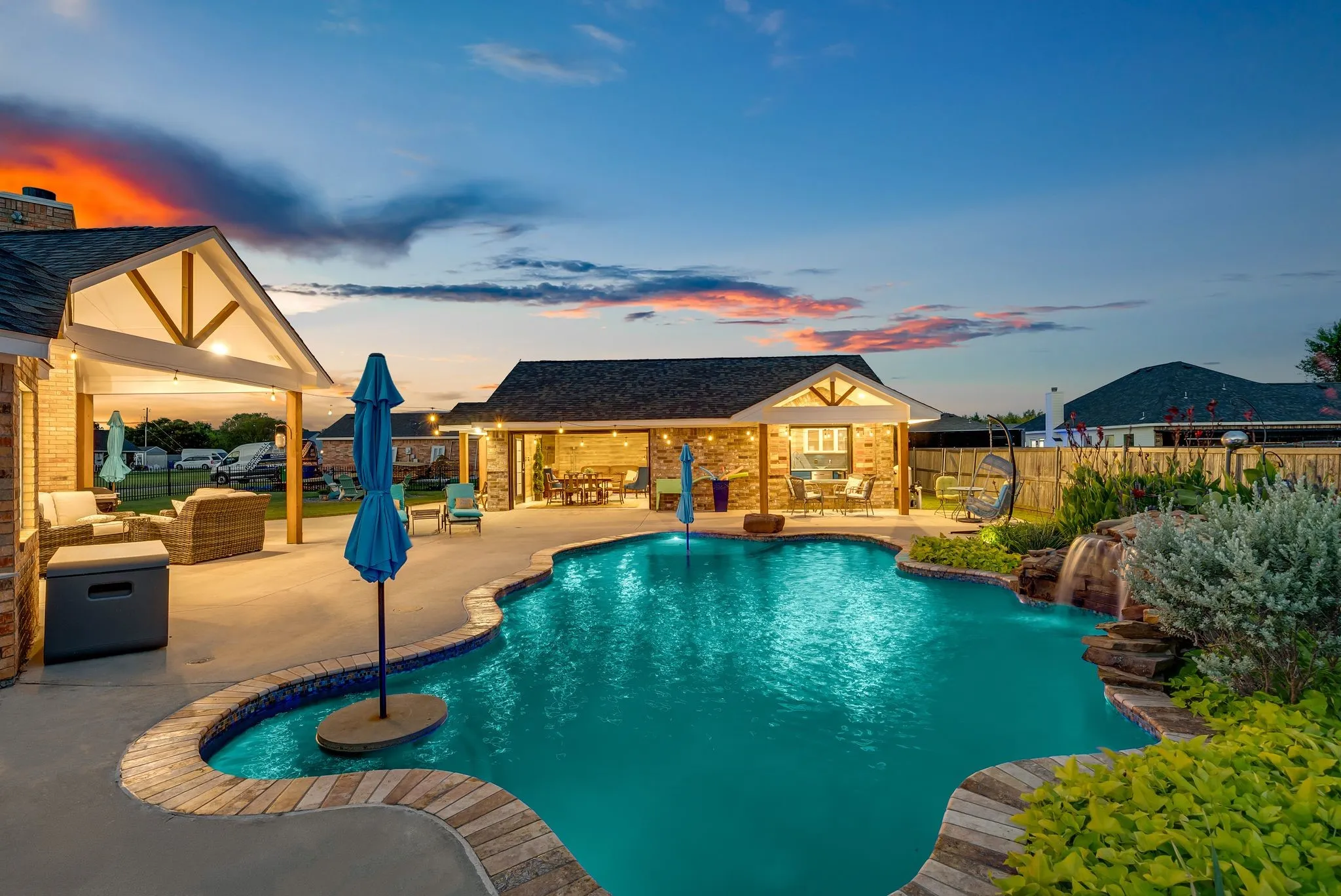 Freeform swimming pool with stone coping and a waterfall feature, complemented by an attached covered patio and a separate pool house structure