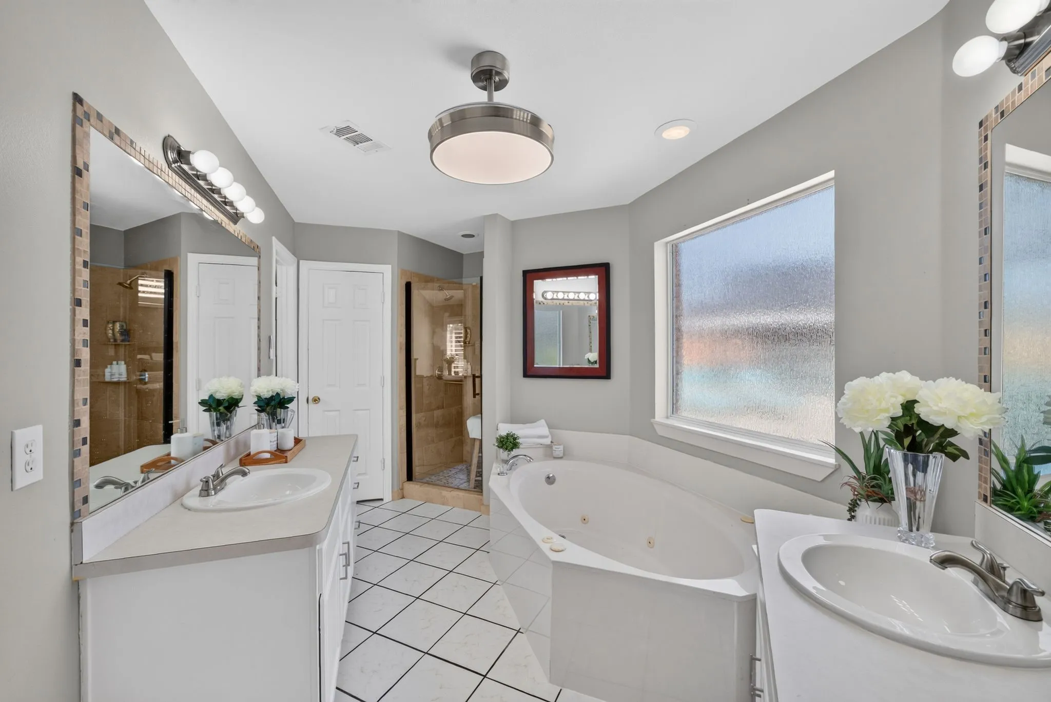 Spacious bathroom featuring a corner jetted tub, dual vanity sinks, and a large frosted window