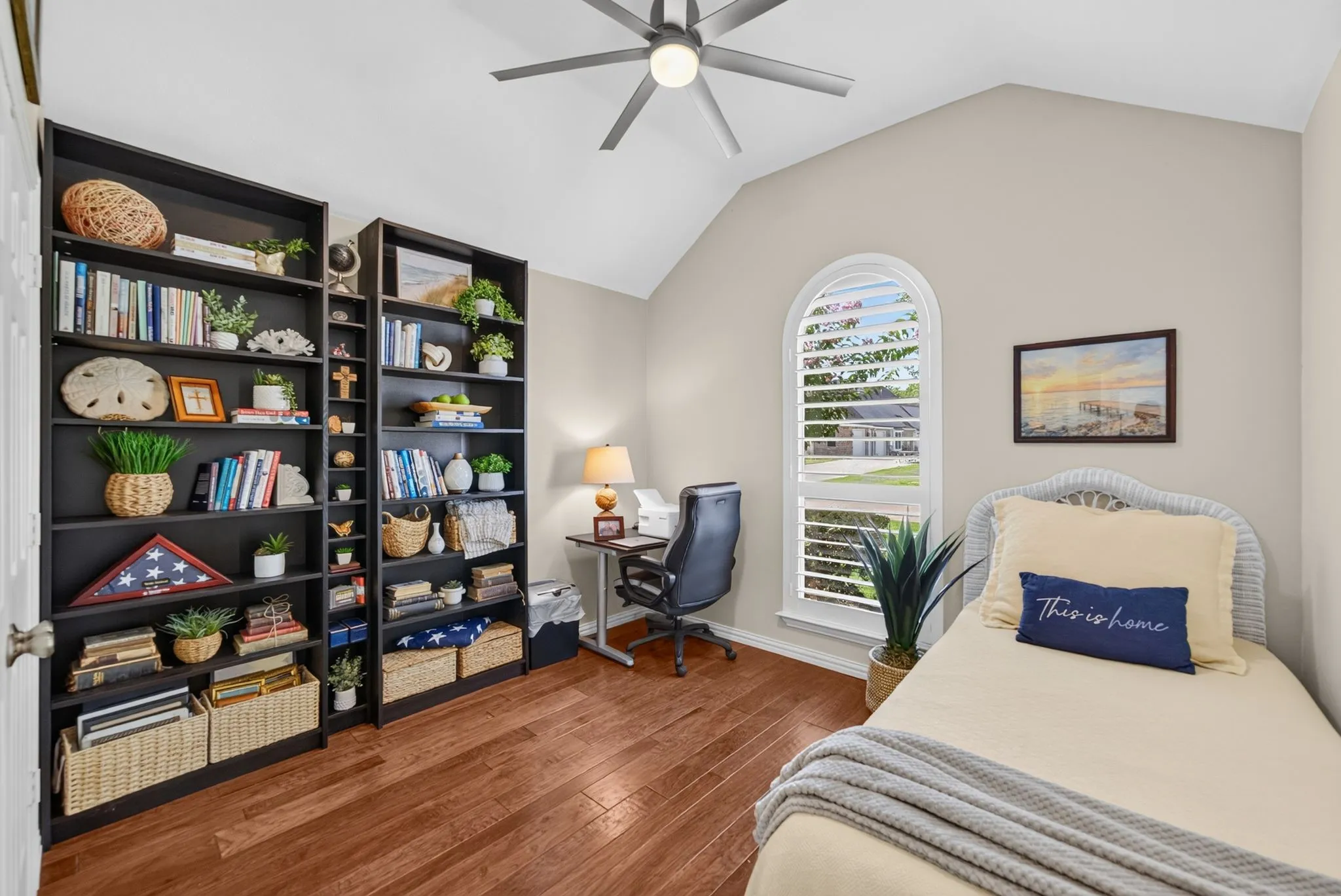 Vaulted ceiling room featuring wood-finish flooring, an arched window with plantation shutters, and built-in shelving