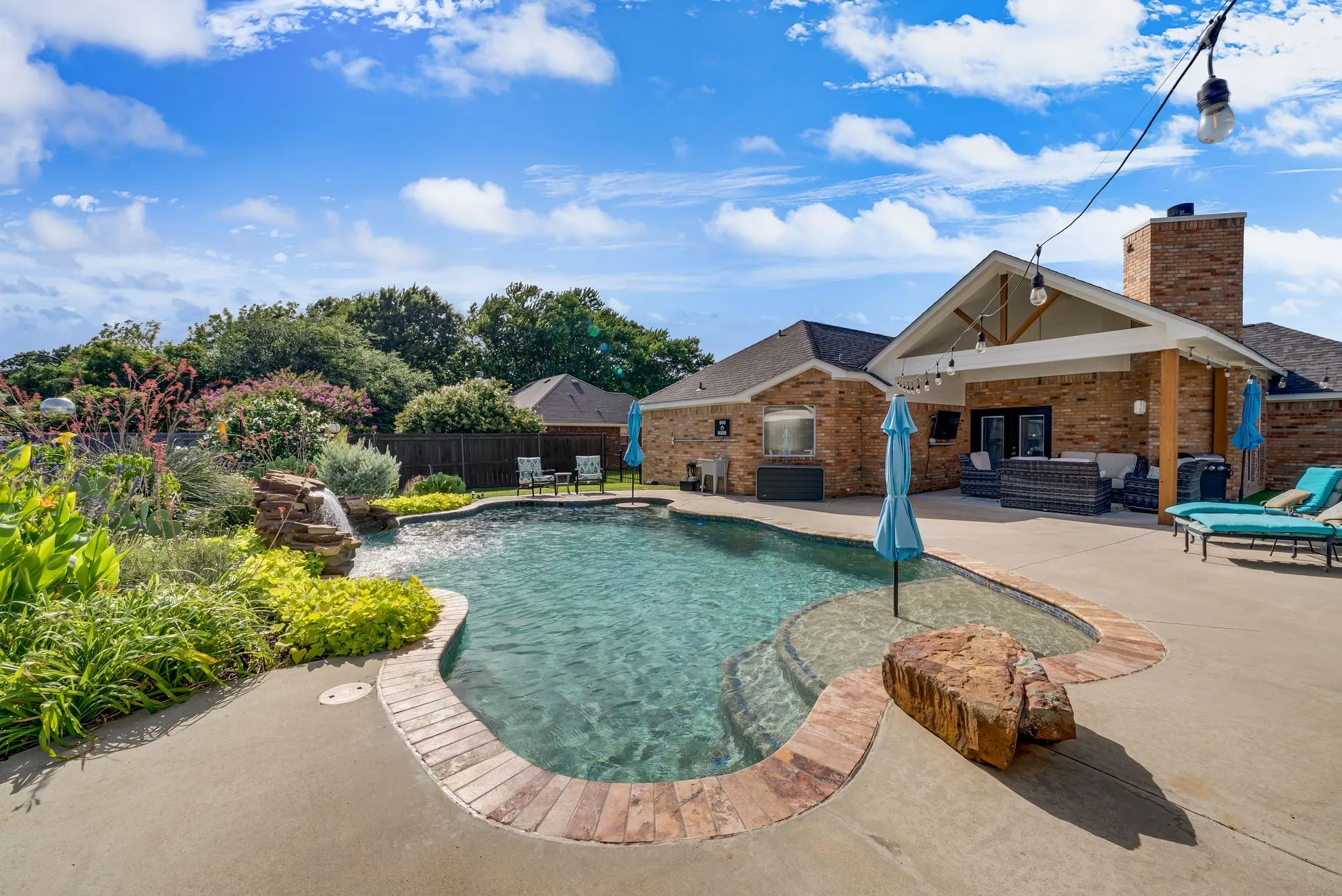 Expansive backyard featuring a freeform swimming pool with a rock waterfall feature and integrated stone steps