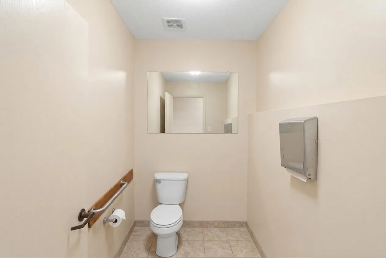 Restroom featuring a white toilet, wall-mounted mirror, ceramic tile flooring, and a towel dispenser