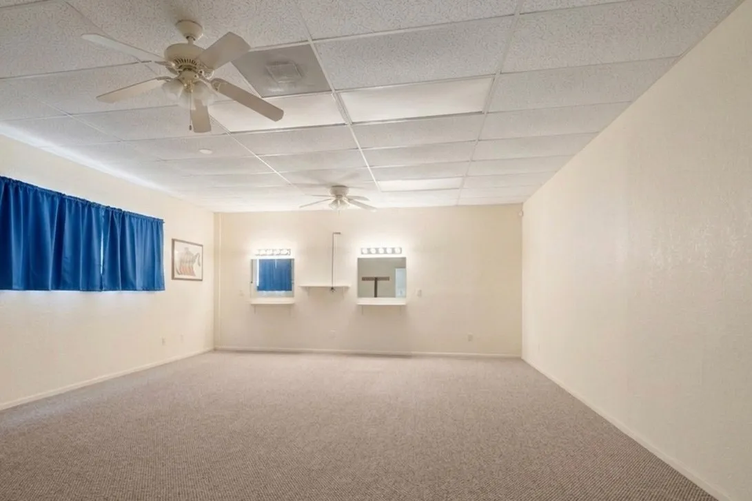 Spacious room featuring neutral carpet flooring, drop ceiling with integrated lighting, and ceiling fans
