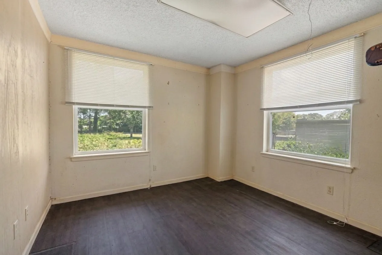 Interior room featuring dark wood-finish flooring, two windows with blinds, and a white ceiling