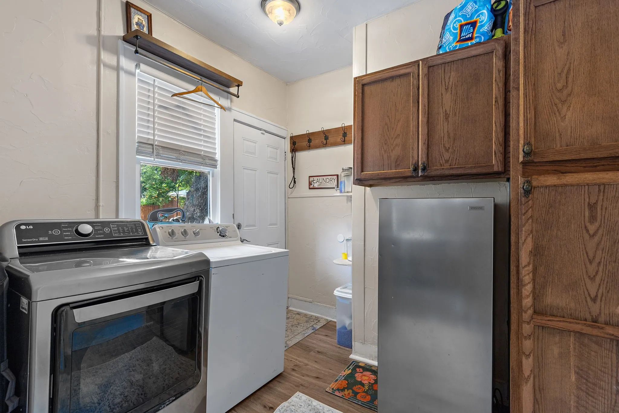 Dedicated utility space with wood-like flooring, a window with blinds, and a paneled door to the backyard