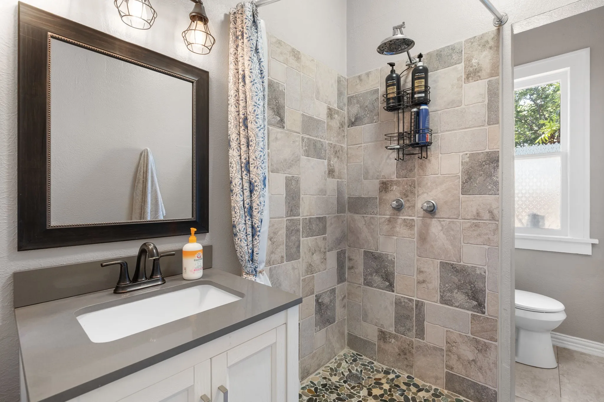 Updated primary bathroom featuring a walk-in shower with varied rectangular tiling and a river rock floor