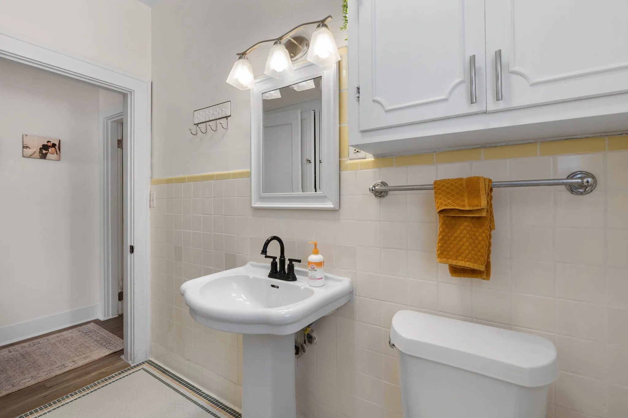 Pedestal sink with a matte black faucet, wall-mounted mirror, and vanity lighting